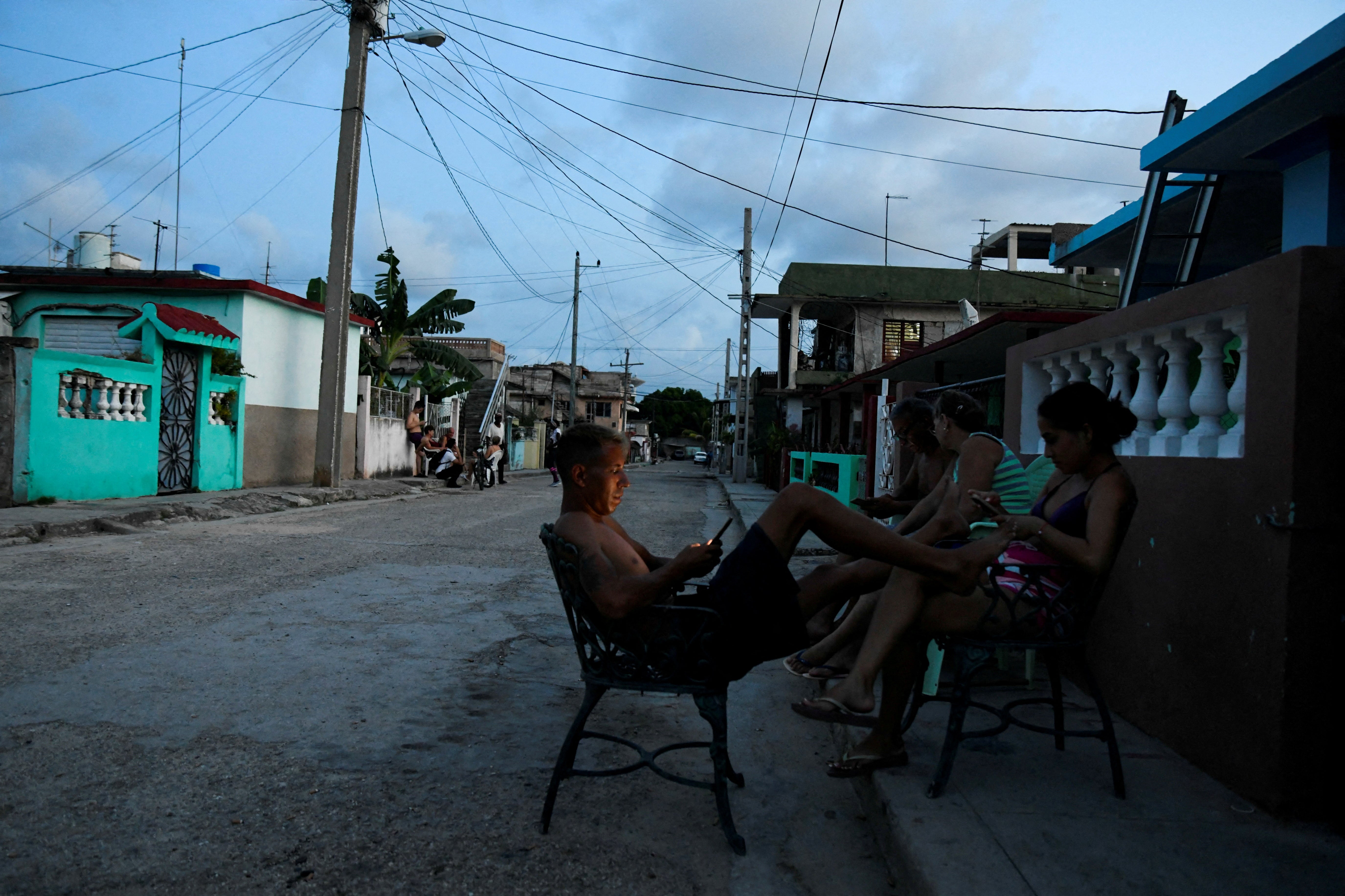 People sit outside their home during a power outage caused by breakdowns forcing six plants to go off-line on the grid