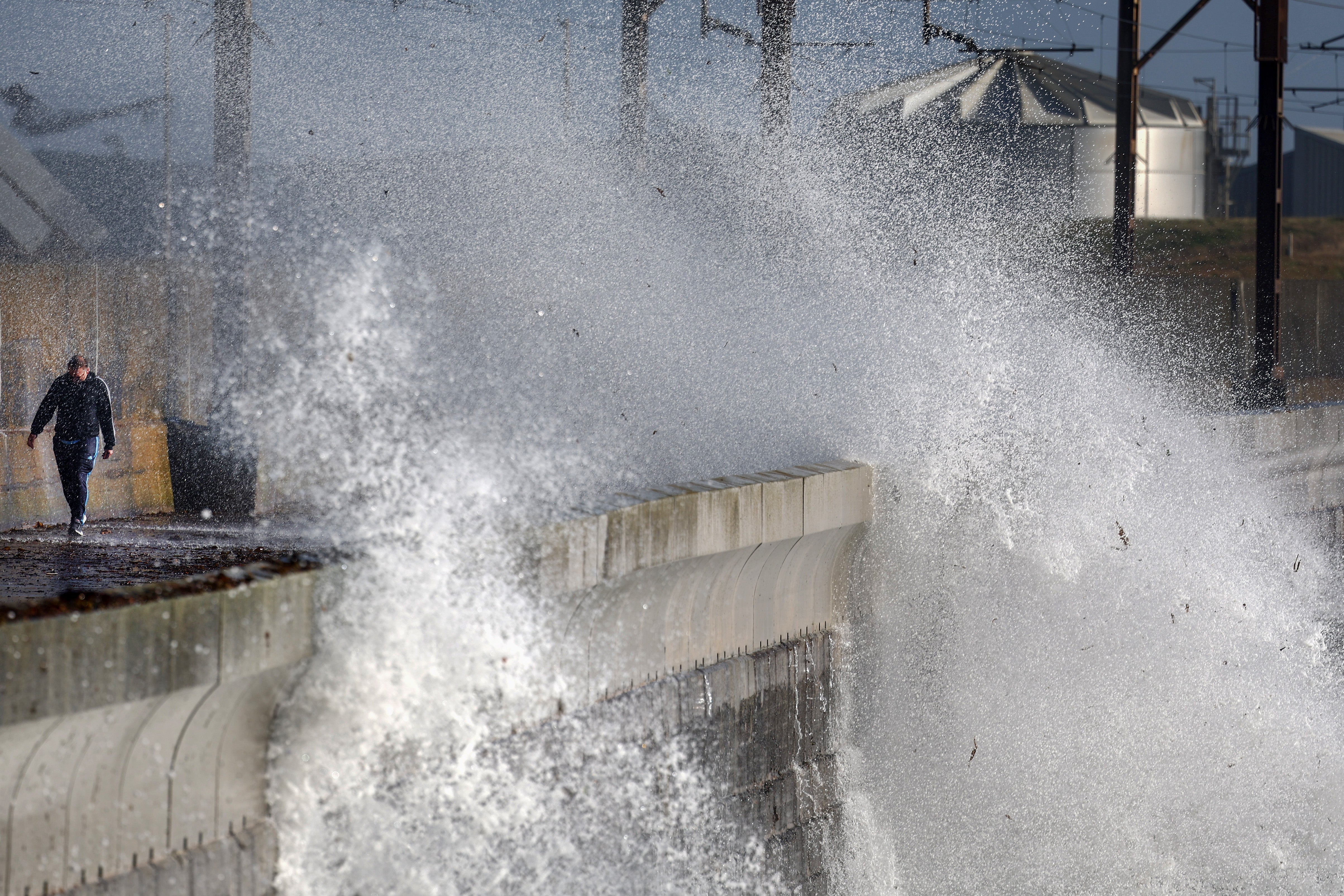 Members of the public walk along a road as waves crash against the sea defences as storm Ashley arrives in Saltcoats, Scotland,