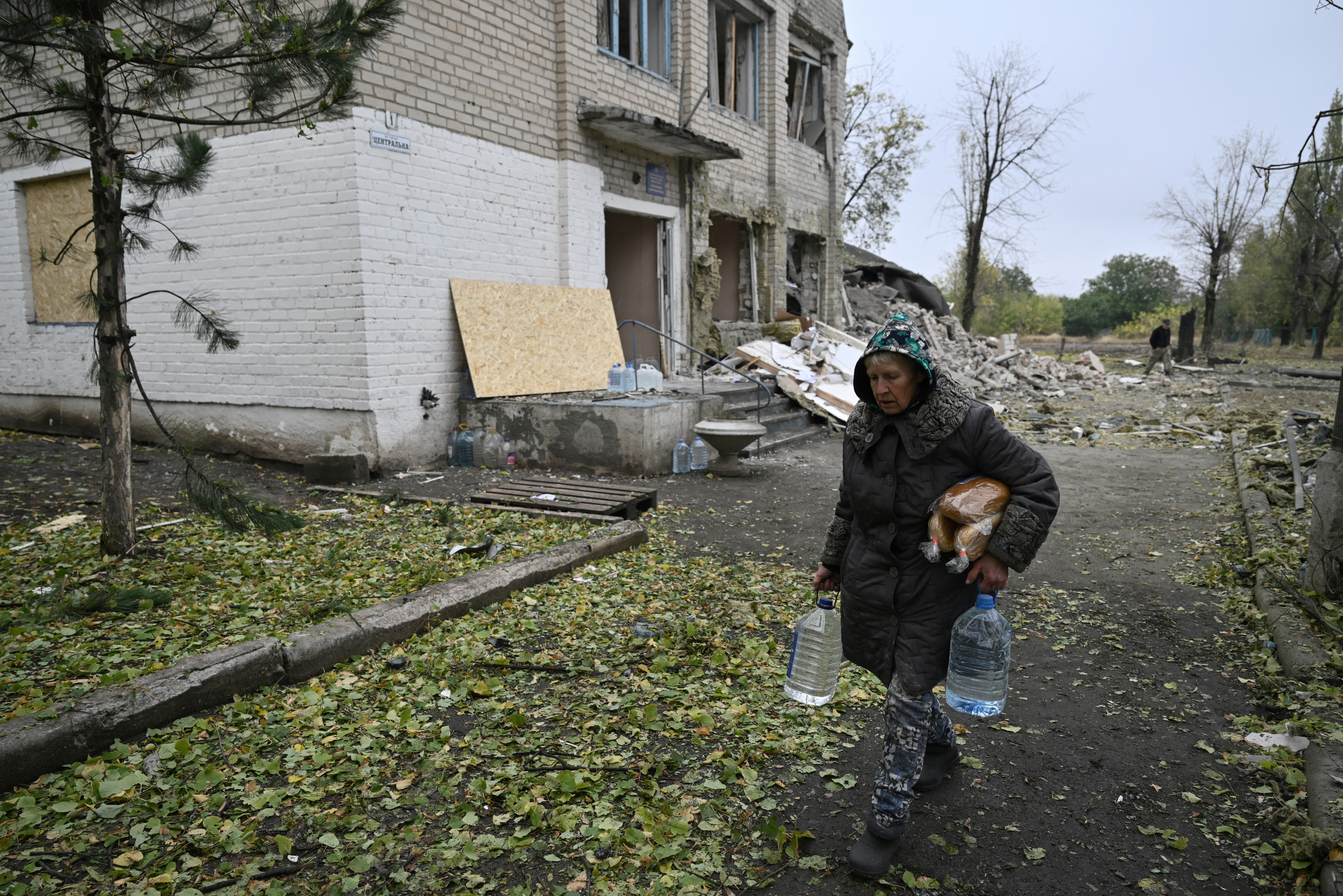 A local resident carries bread and water as she walks past a local administrative building, destroyed following Russian strike in the village Shevchenko, near the city of Pokrovsk, Donetsk