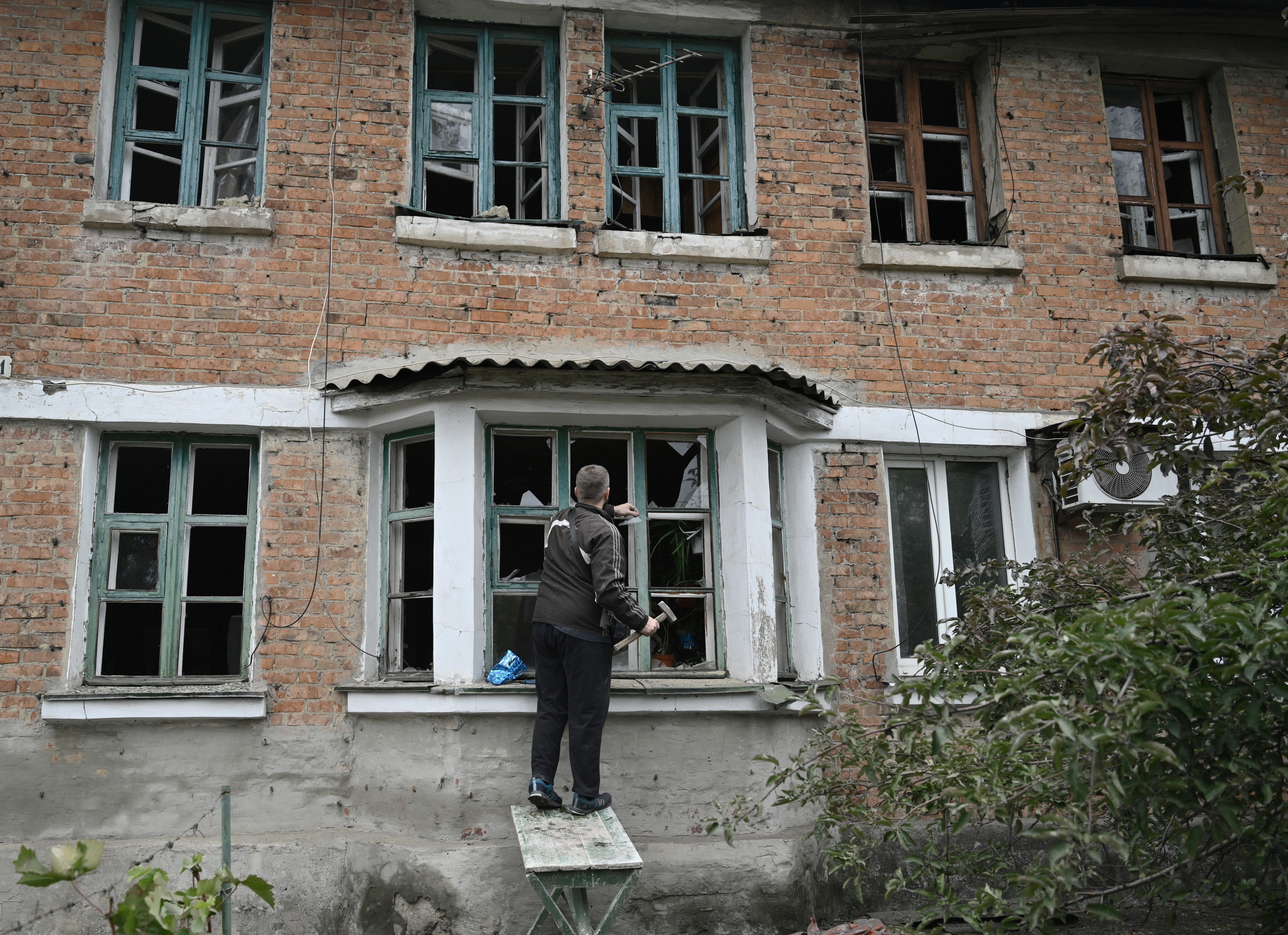 A local resident clears the shattered glass in a broken window in a residential building following Russian strike in Shevchenko village