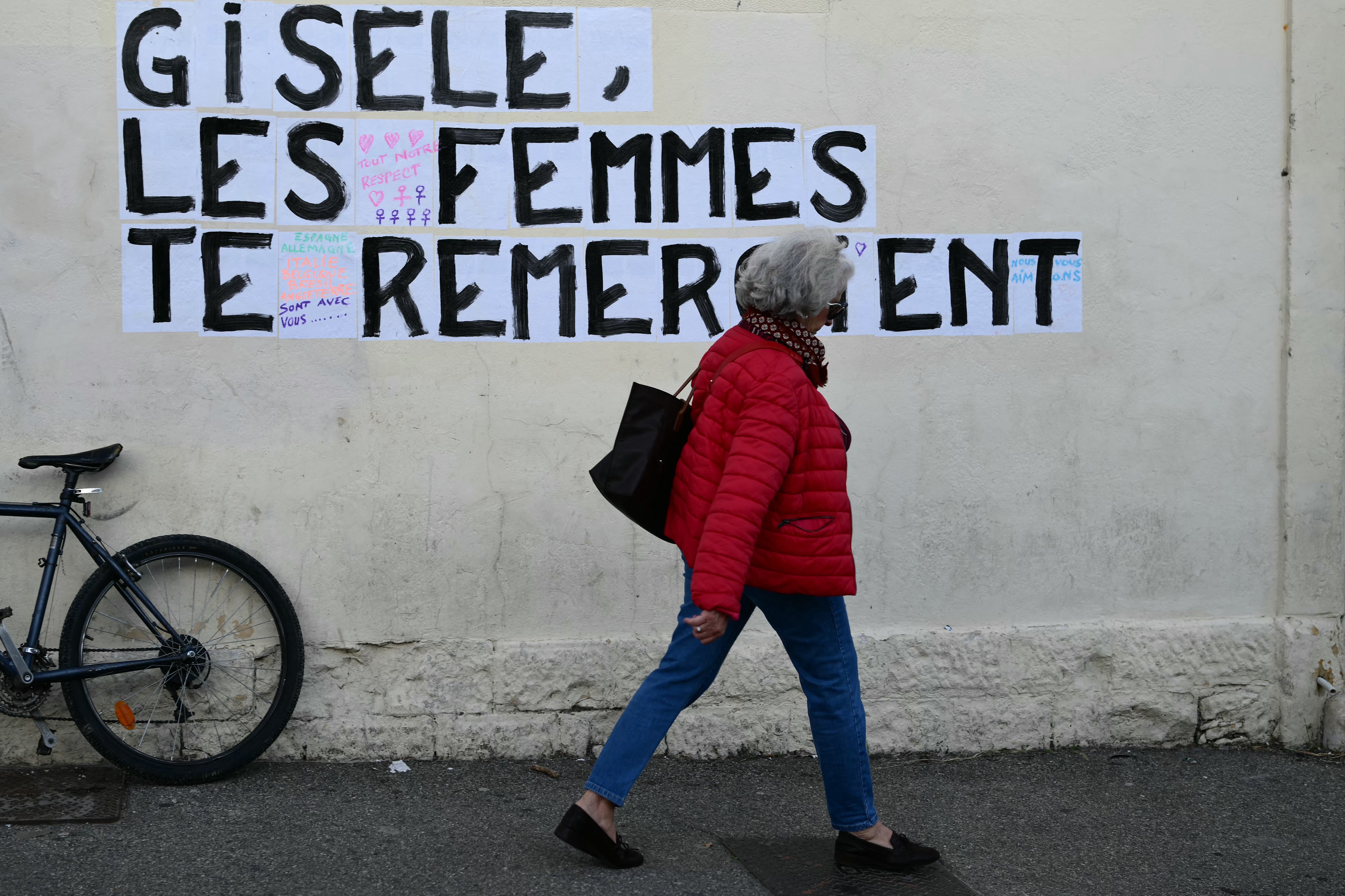 A pedestrian walks past a collage-mural reading “Gisele, women thank you” near the Avignon courthouse