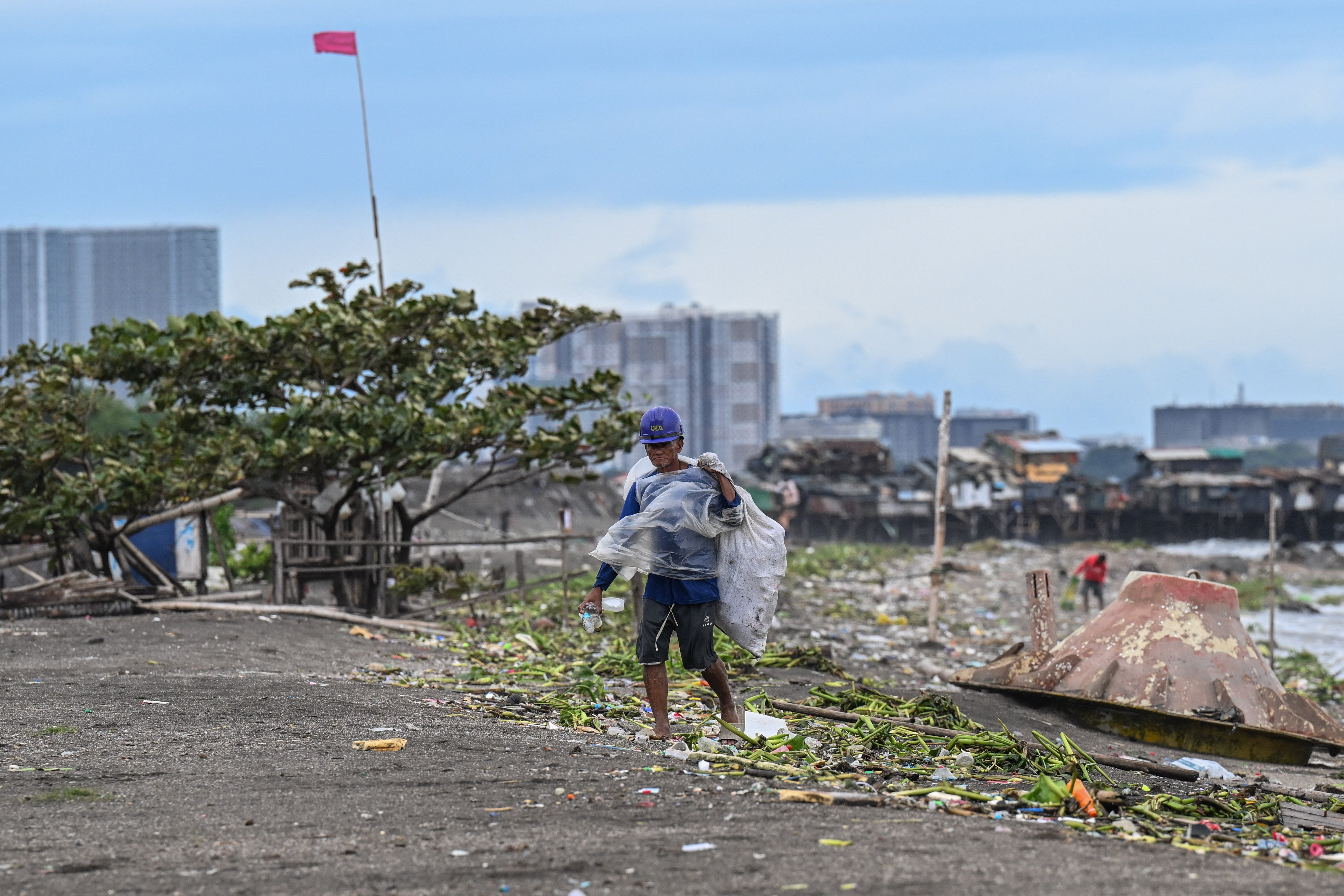 A man wearing a raincoat collects trash through strong winds brought by Trami in Manila on 23 October 2024