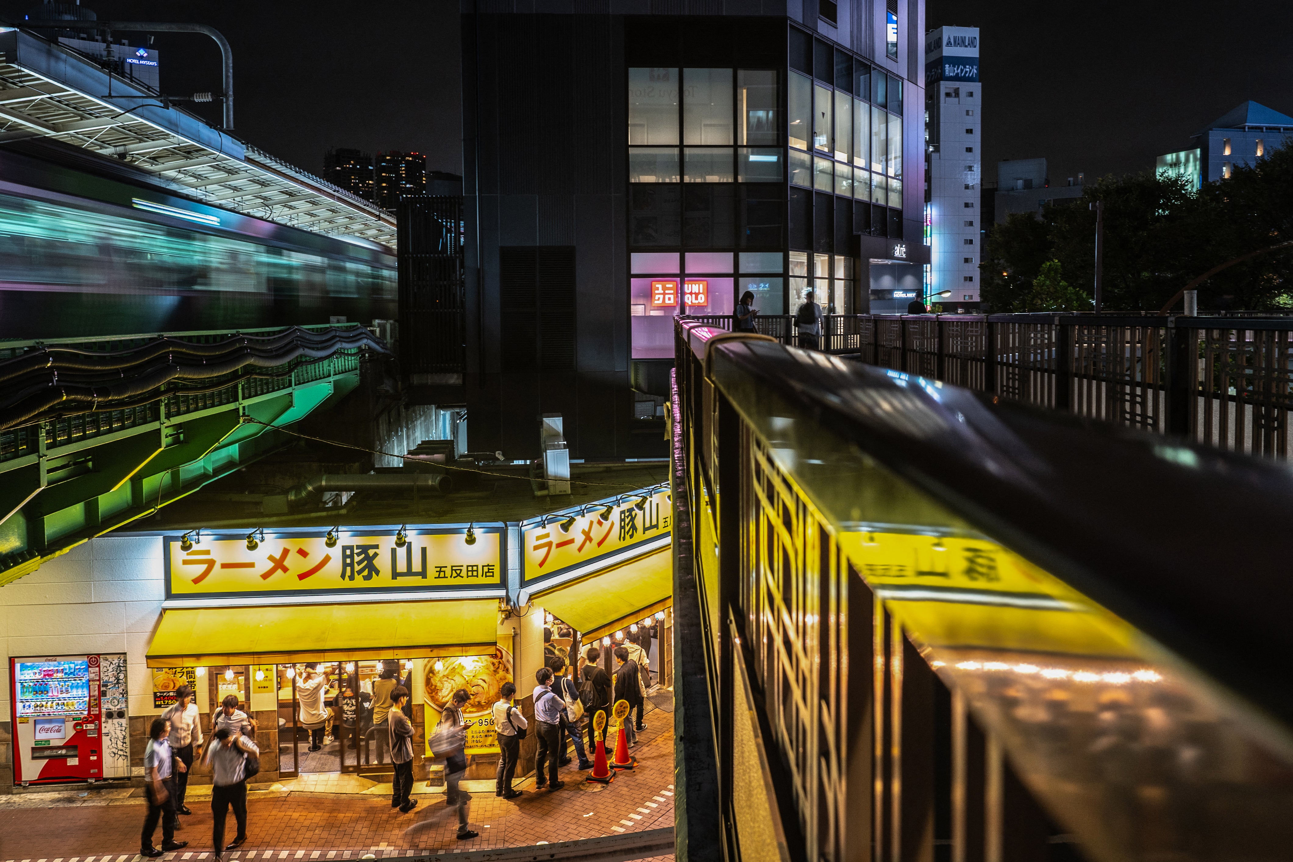 People line up to enter a ramen shop (C) as a train (L) departs from Gotanda station in Tokyo on October 4, 2024