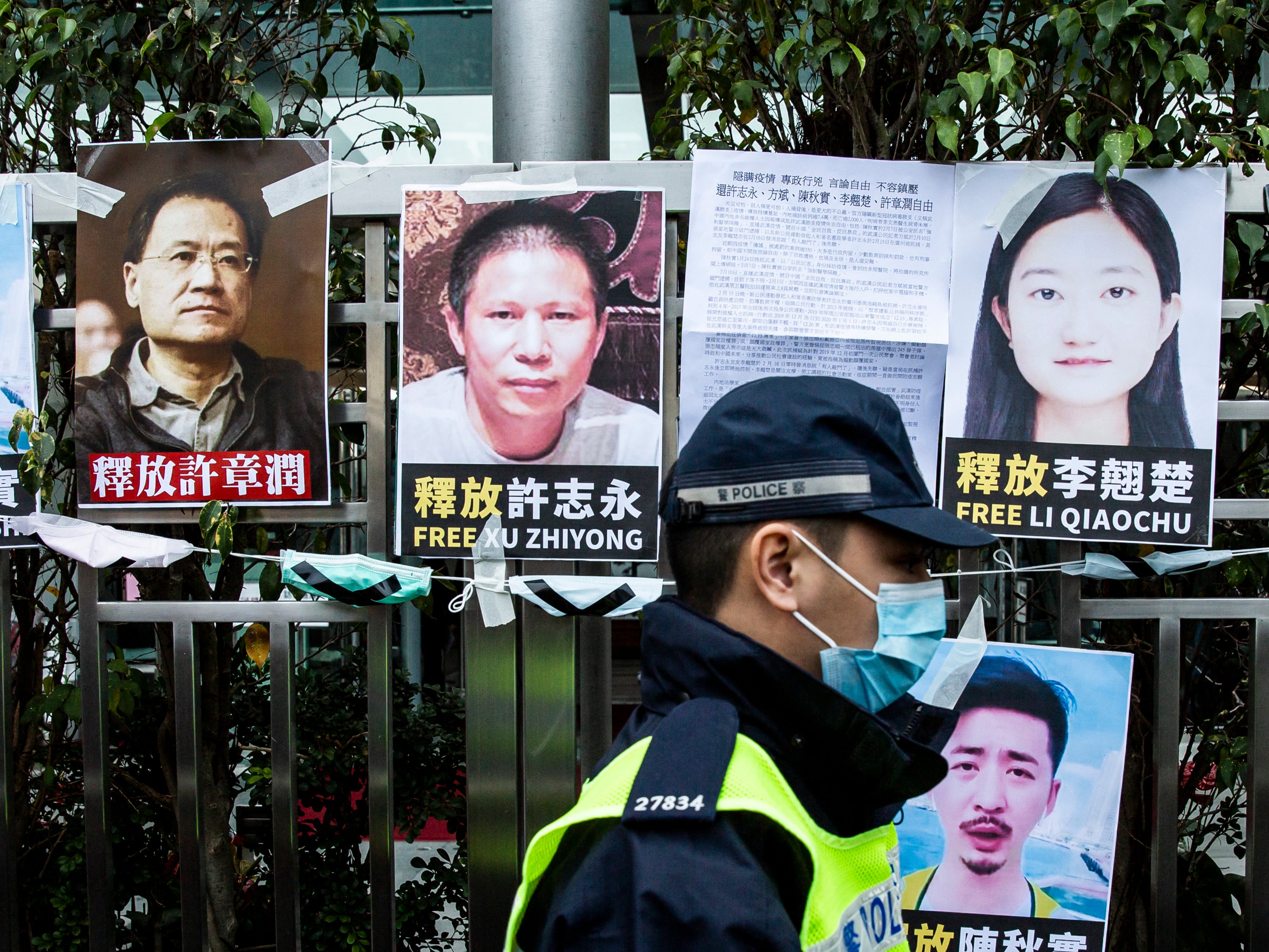 Police officer walks past posters of detained activists put up on a fence of the Chinese liaison office in Hong Kong