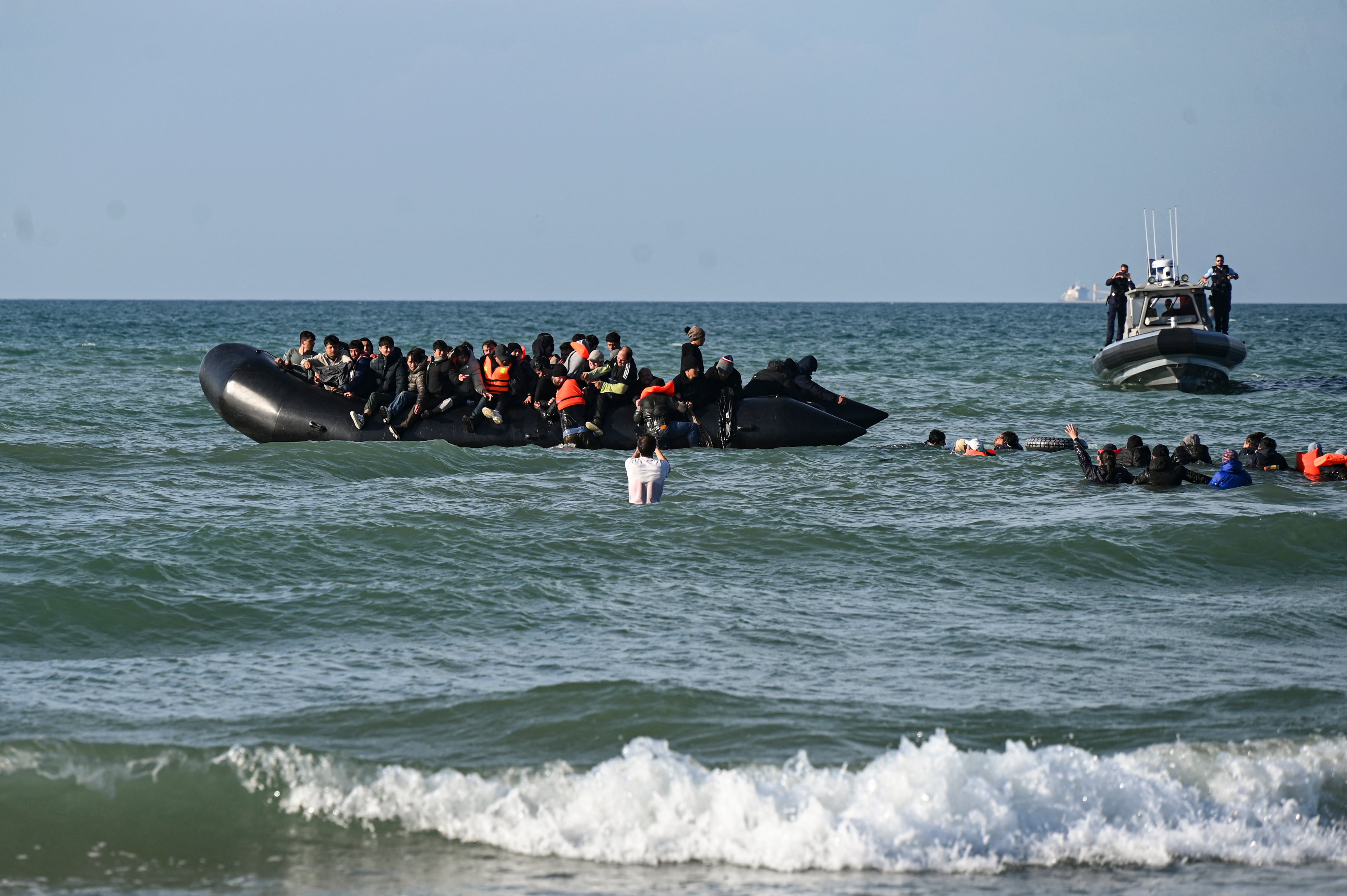 Migrants swim to board a smugglers' boat in order to attempt crossing the English channel off the beach of Audresselles, northern France on October 25, 2024