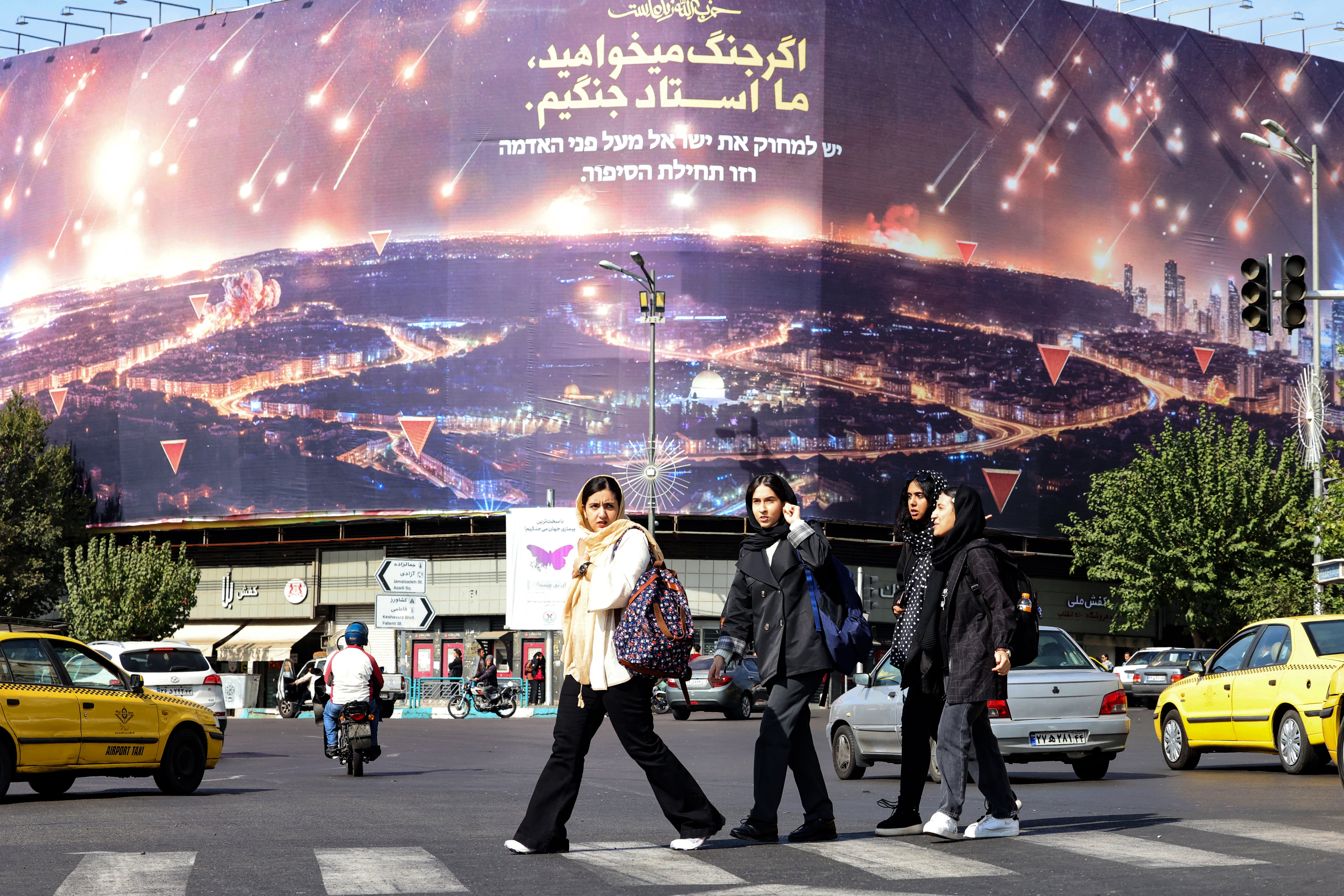 Women walk past an anti-Israel billboard covering the facade of a building in Tehran on 26 October 2024