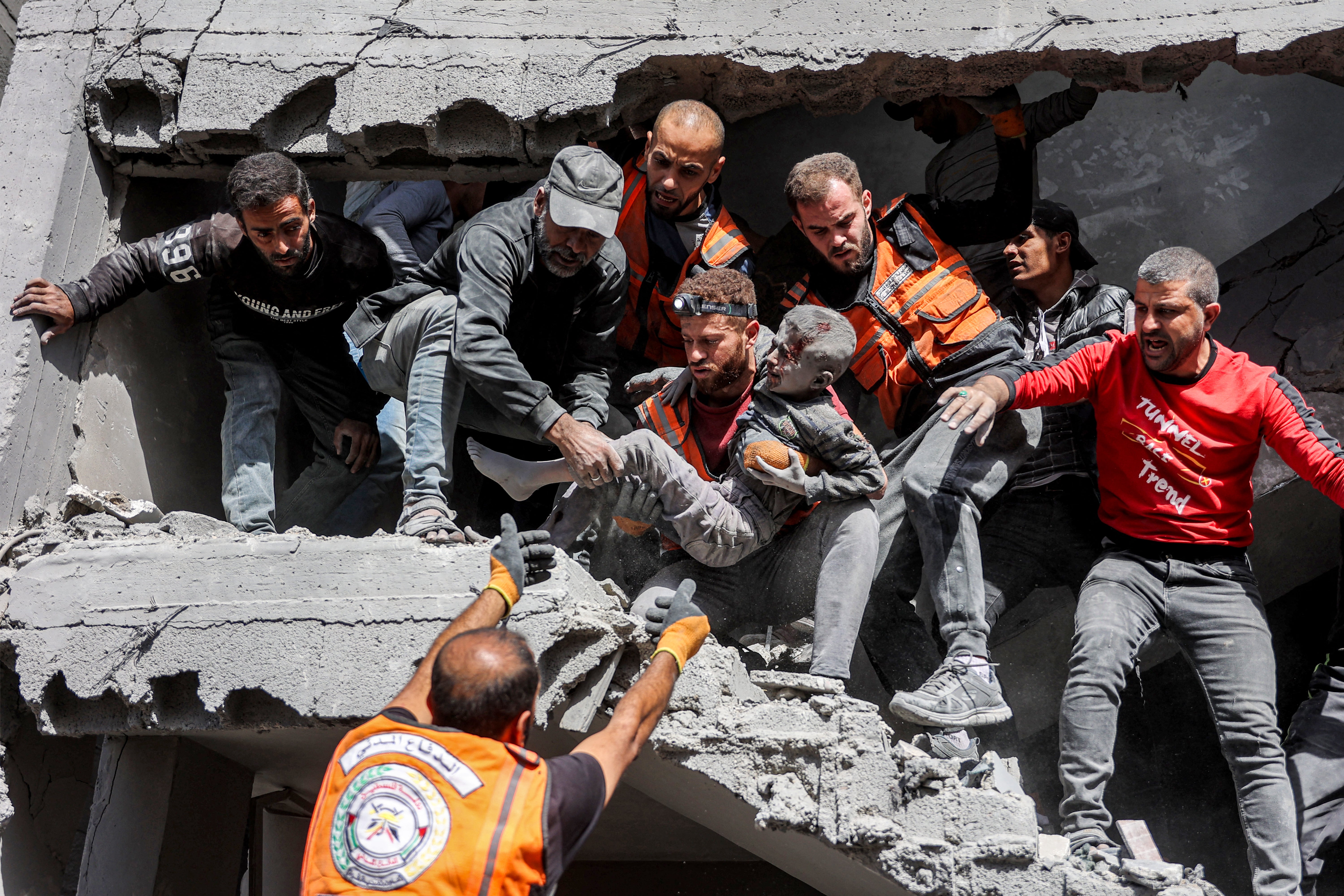 Palestinian civil defence members hand over to each other a child that was rescued following Israeli bombardment in Gaza on 26 October 2024