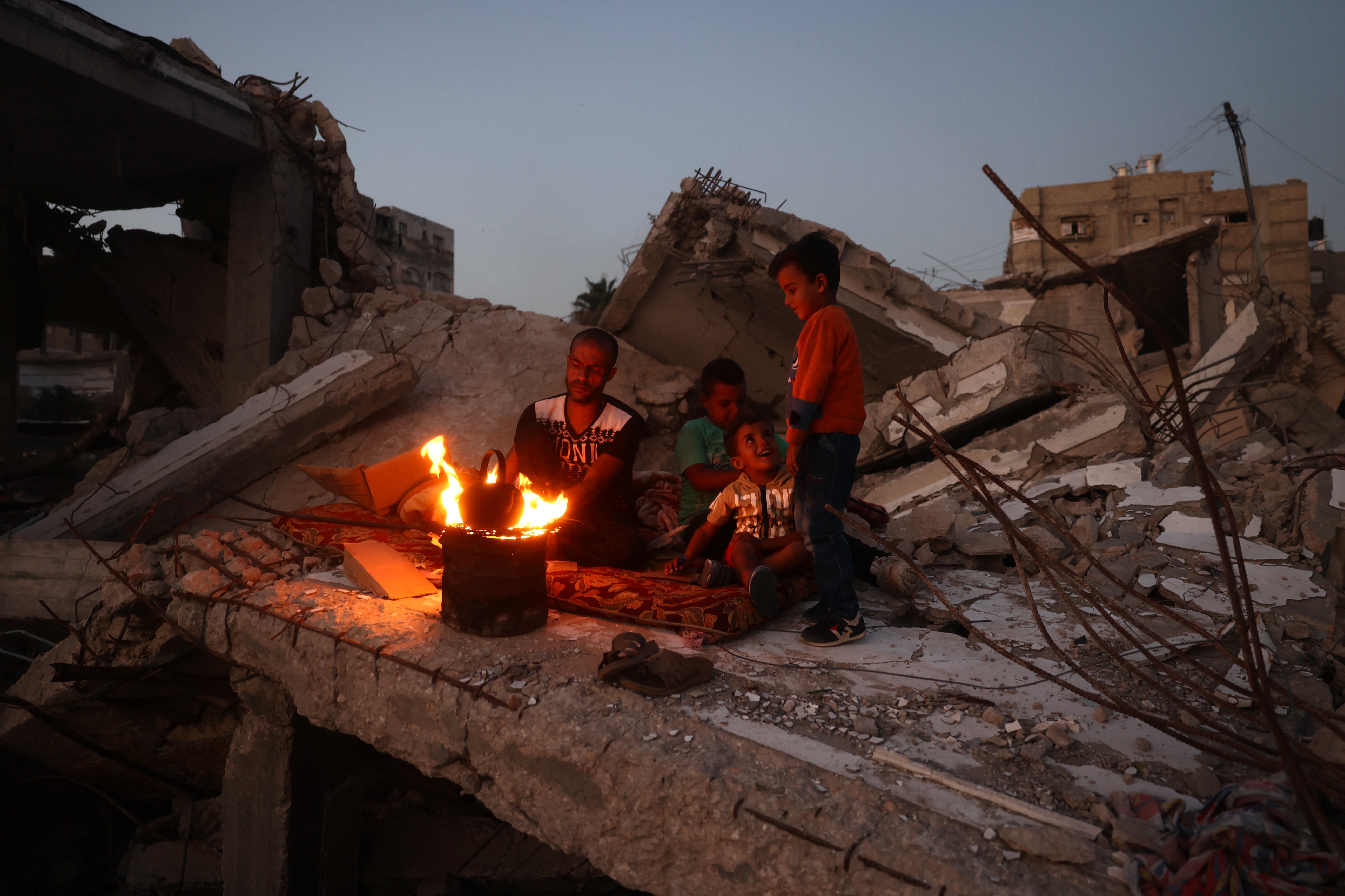 A Palestinian man make tea with his children on the rubble of their home in the Bureij camp for Palestinian refugees in the central Gaza Strip