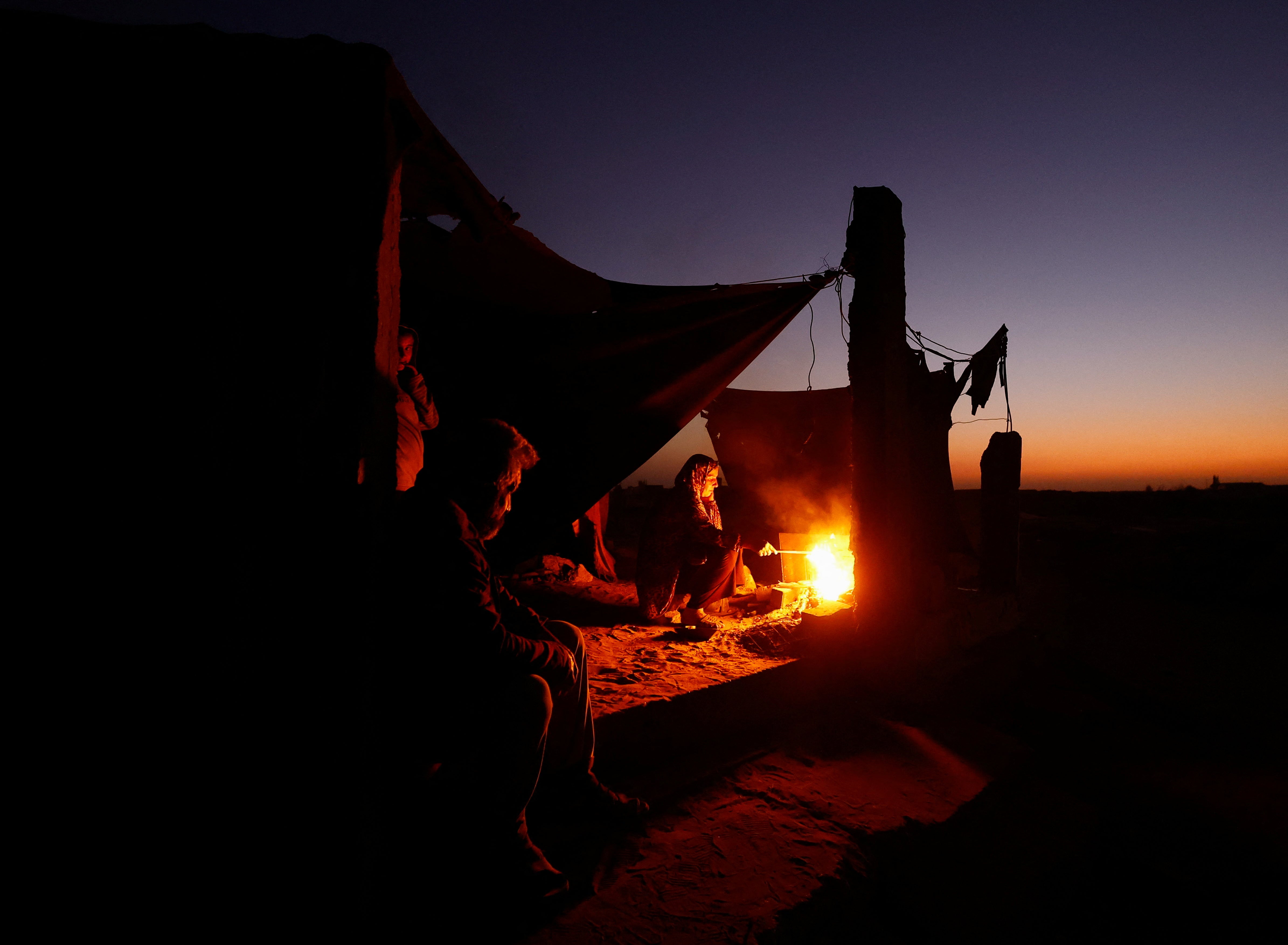 Displaced Palestinian light a fire next to their tent as they live at a cemetery in Khan Younis, in the southern Gaza Strip