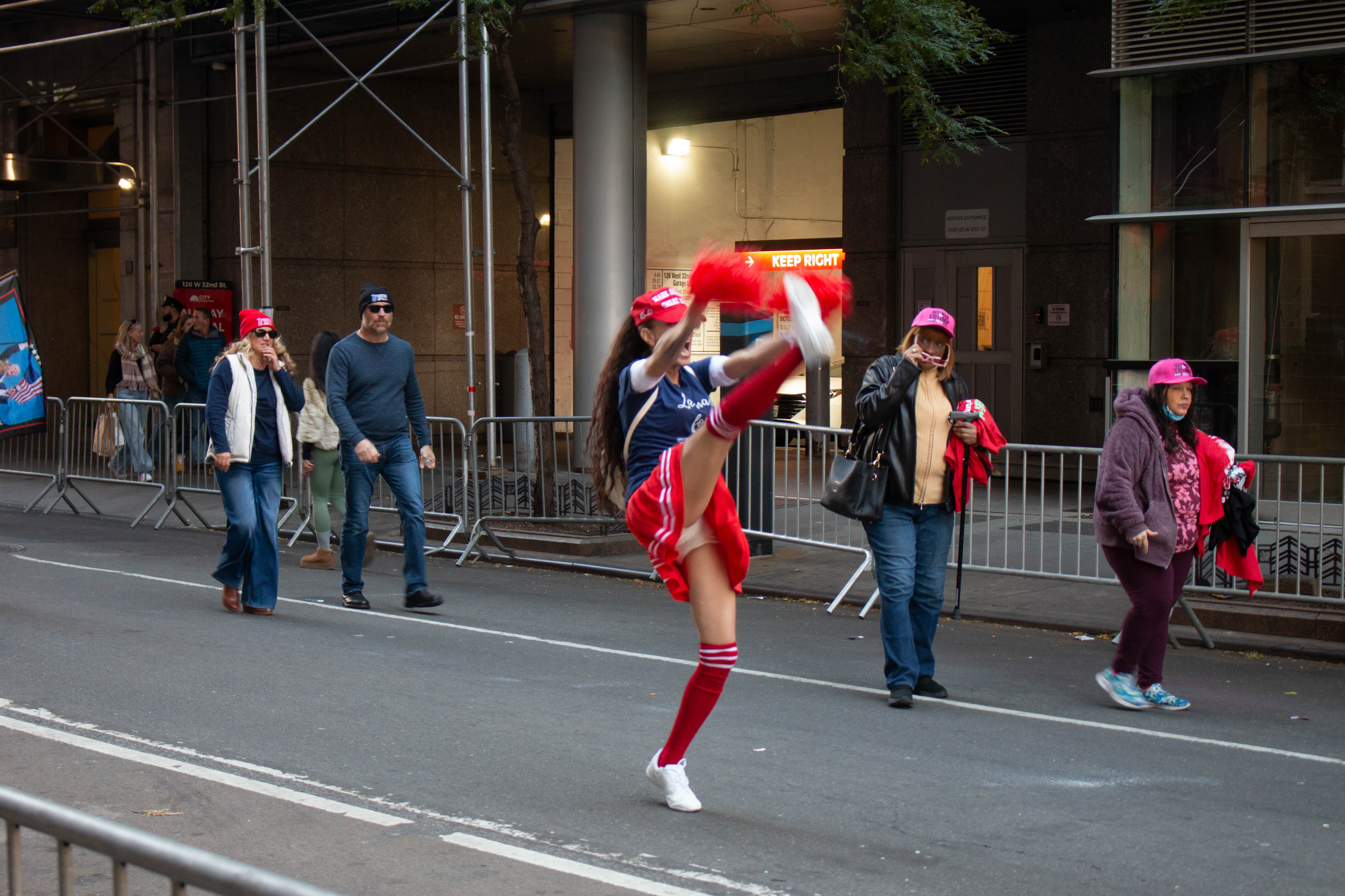 A Trump supporter wears a cheerleading outfit and kicks her legs while screaming “Trump!” in Midtown Manhattan