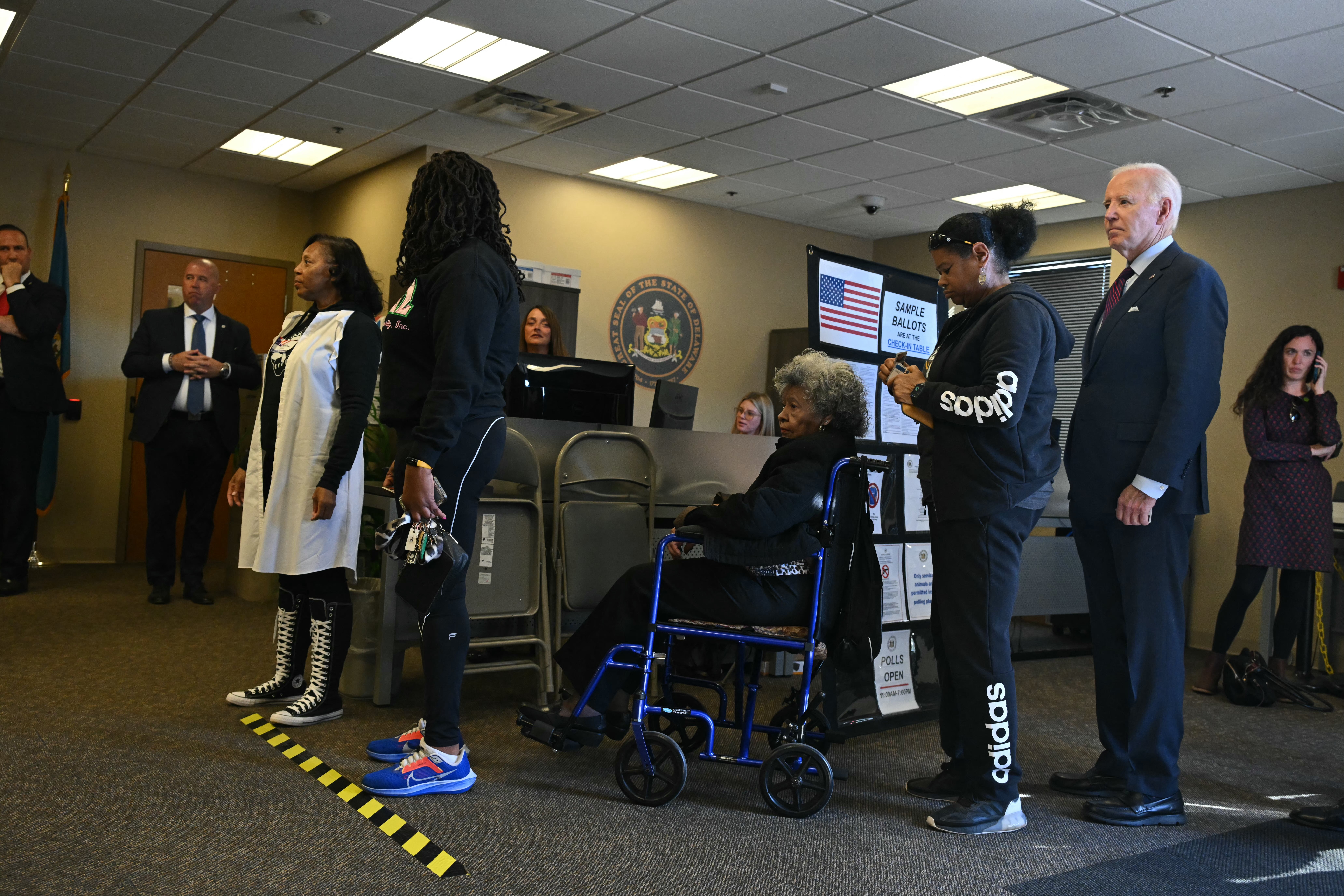 US President Joe Biden (R) waits in line with voters inide a polling station in New Castle, Delaware, October 28, 2024.