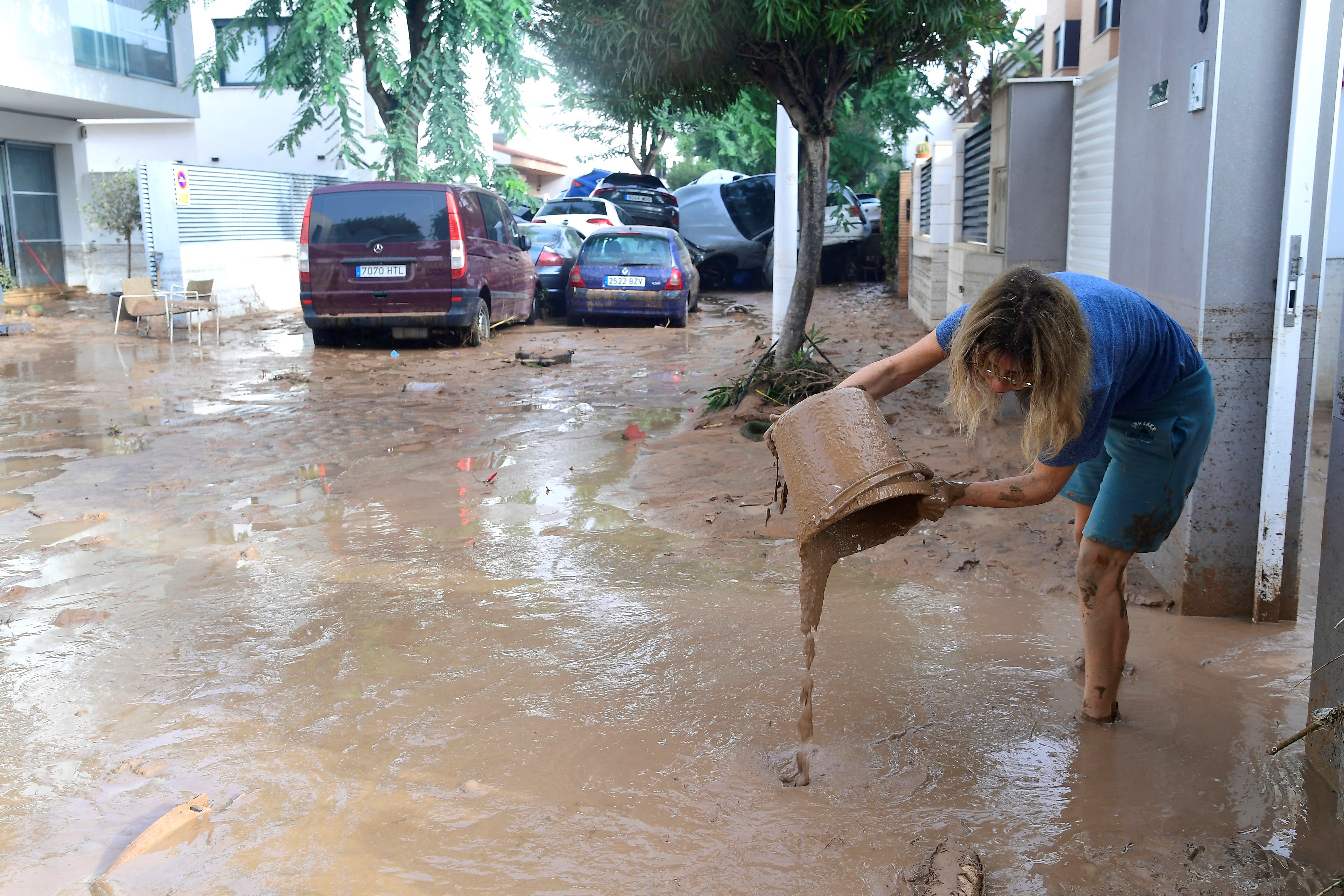 A resident cleans her house next to cars piled up due to mudslide in the flooded area in Picuana