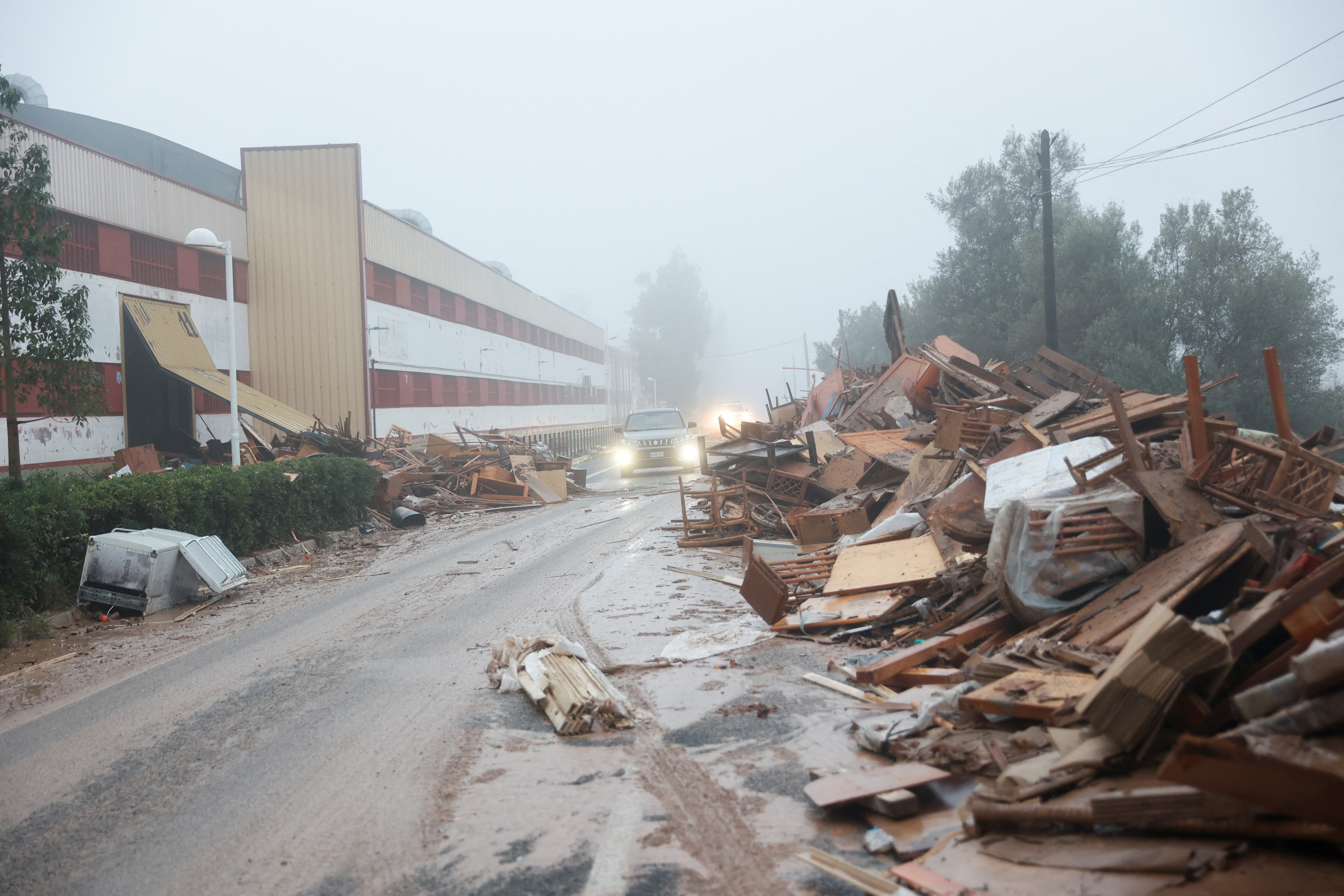 A car drives past damaged items from a furniture factory affected by the flooding in La Alcudia, Valencia