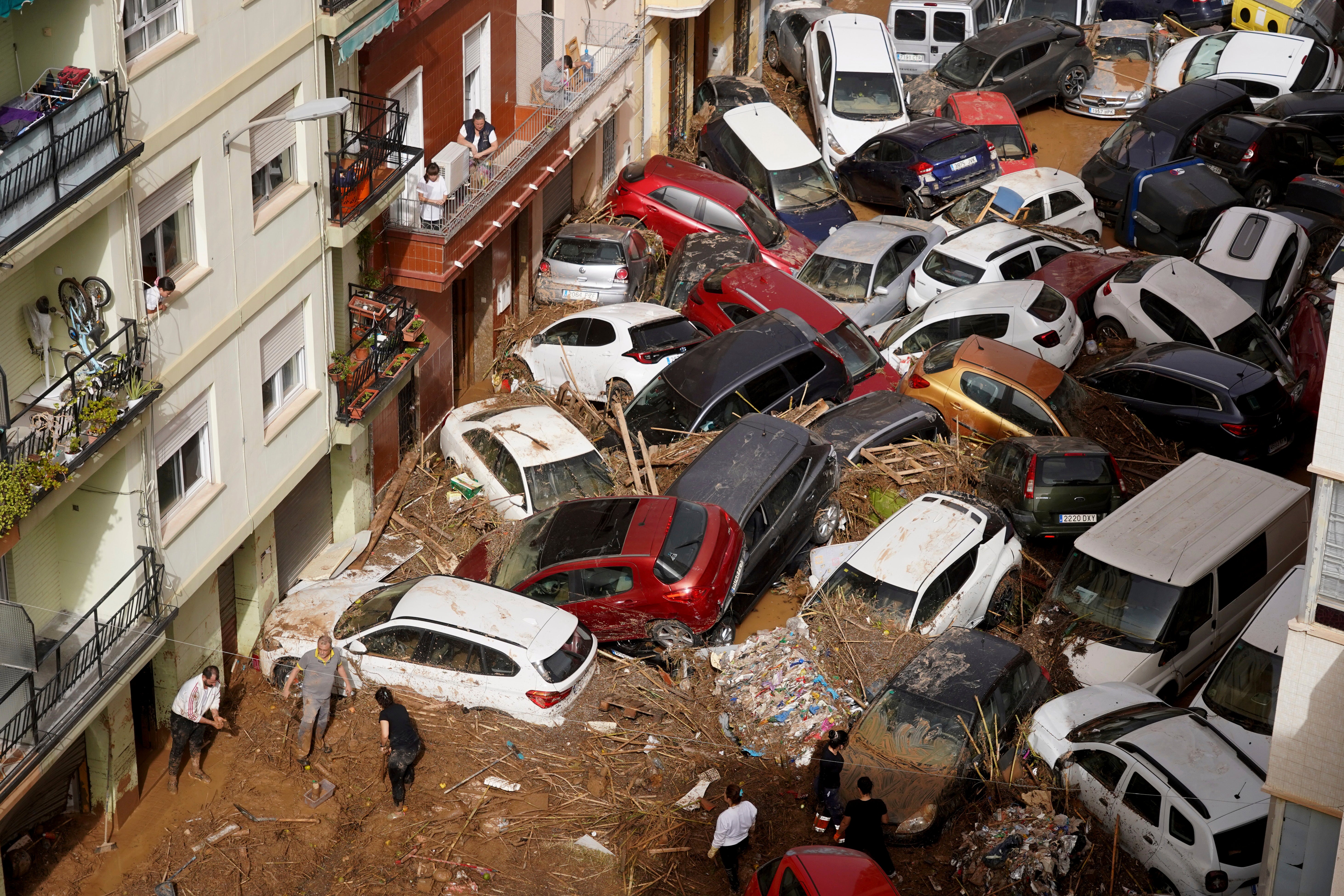 Residents clean the street next to cars piled up after being swept away by floods in Valencia