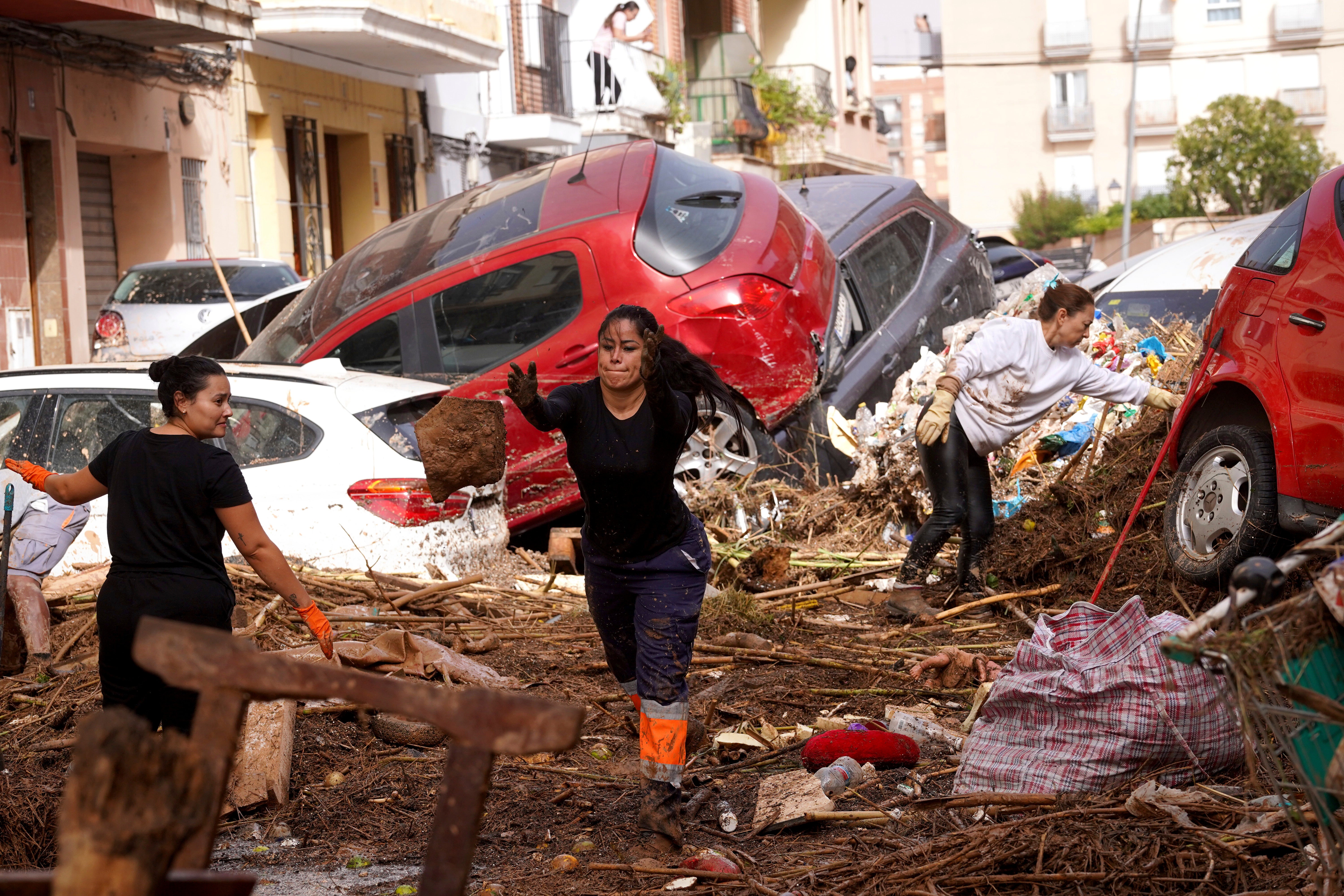 Residents clean the street next to cars piled up after being swept away by floods in Valencia