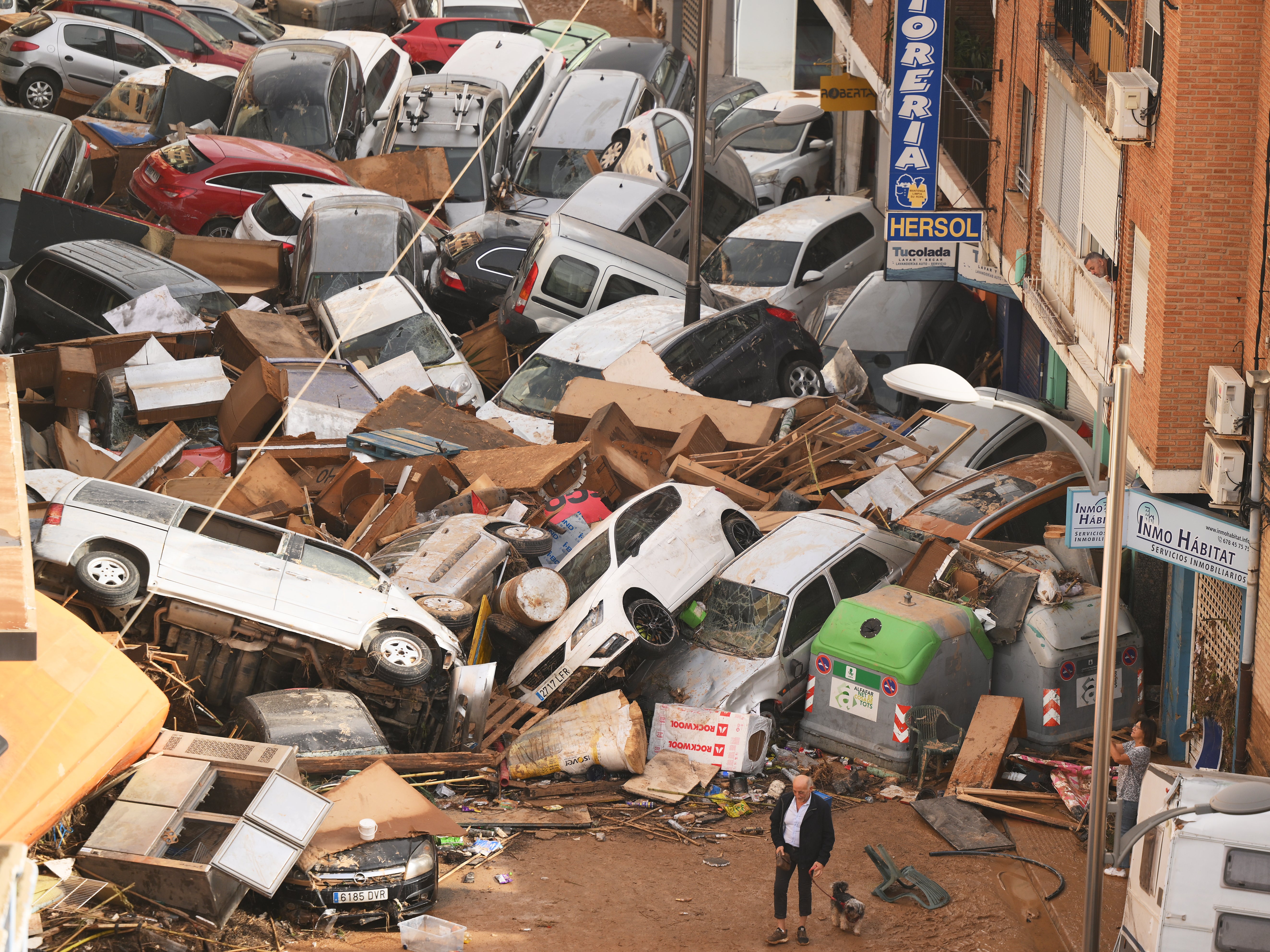 cars piled high in a street, overshadowing a man and dog