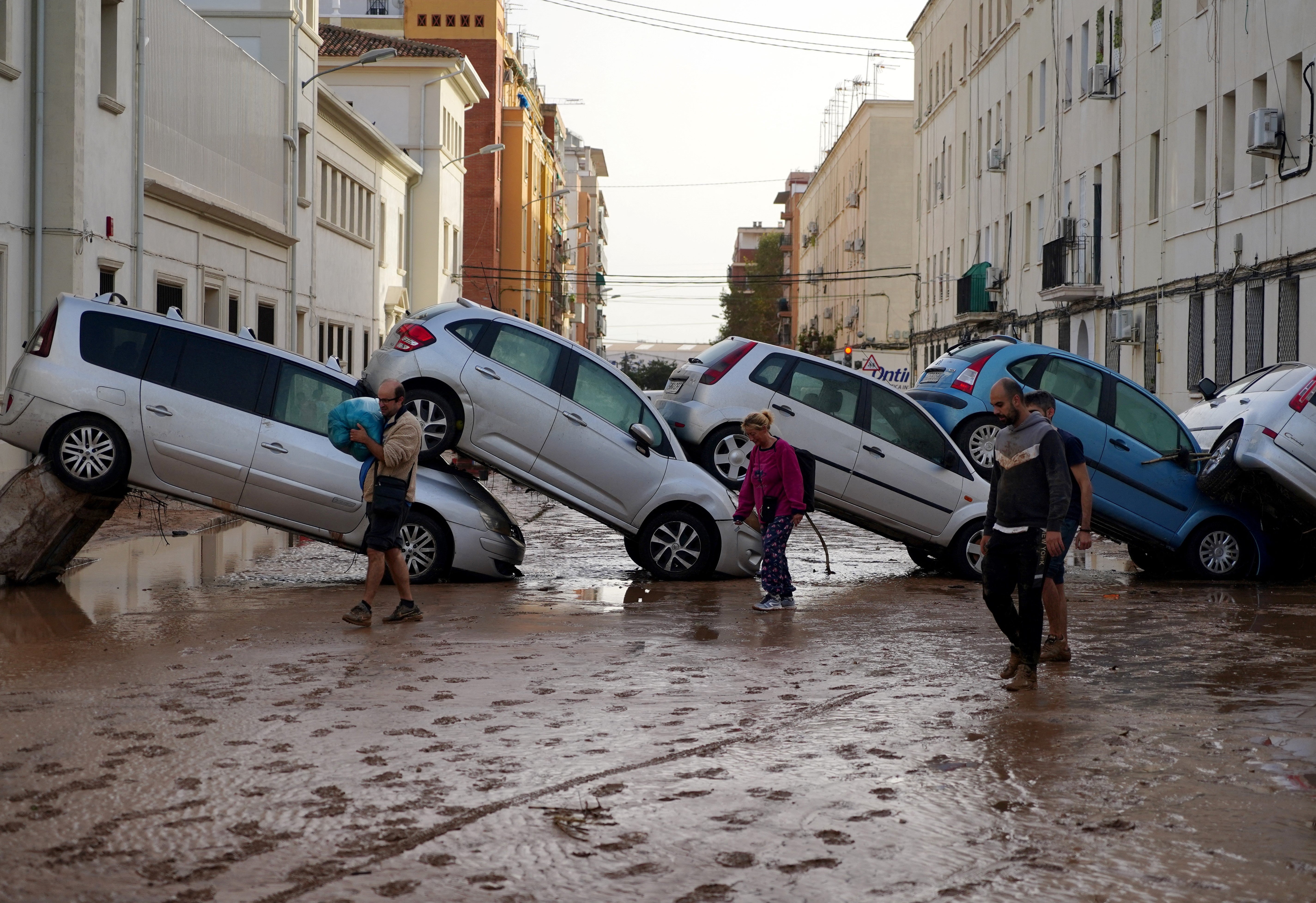 Residents walk past piled up cars following deadly floods in Valencia’s De La Torre neighbourhood, south of Valencia