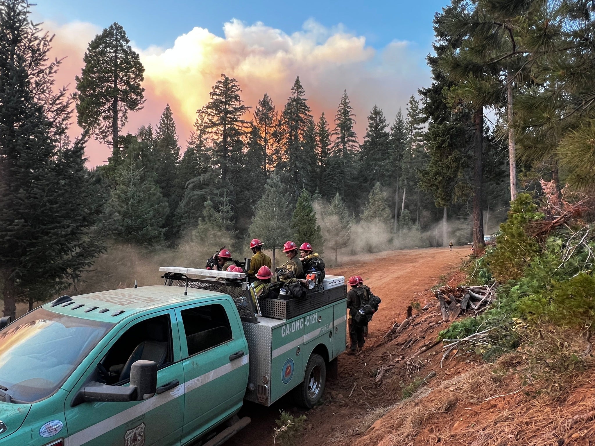 California firefighters sit on the back of a truck near plumes from the Park Fire last July. The Park Fire tore across nearly 43,000 acres, becoming the state’s fourth-largest fire in history.