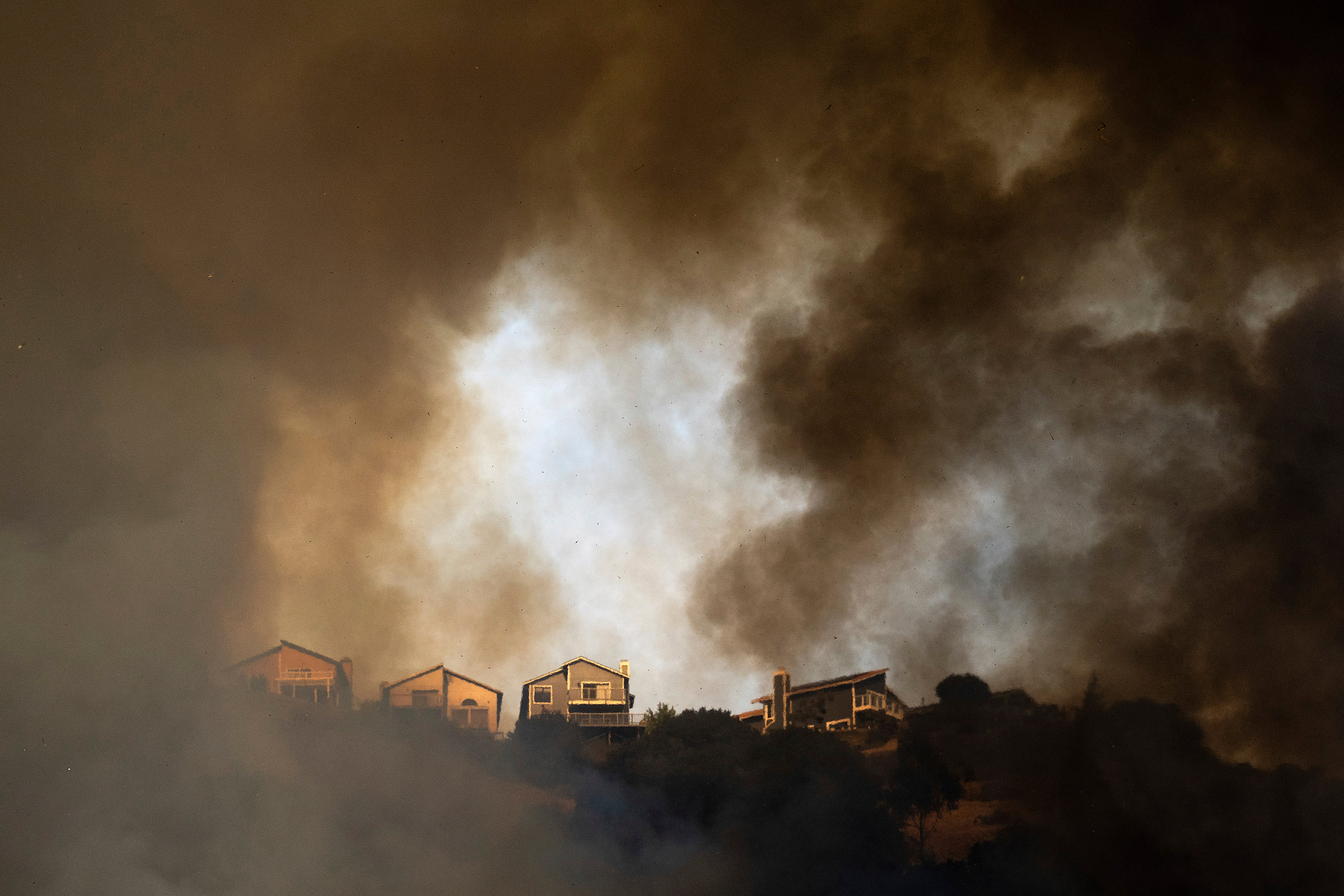 Smoke rises above homes as a grass fire burns near Interstate 580 in Oakland, California, last month. Climate change has fueled windy, hot, and dry conditions late into fall.