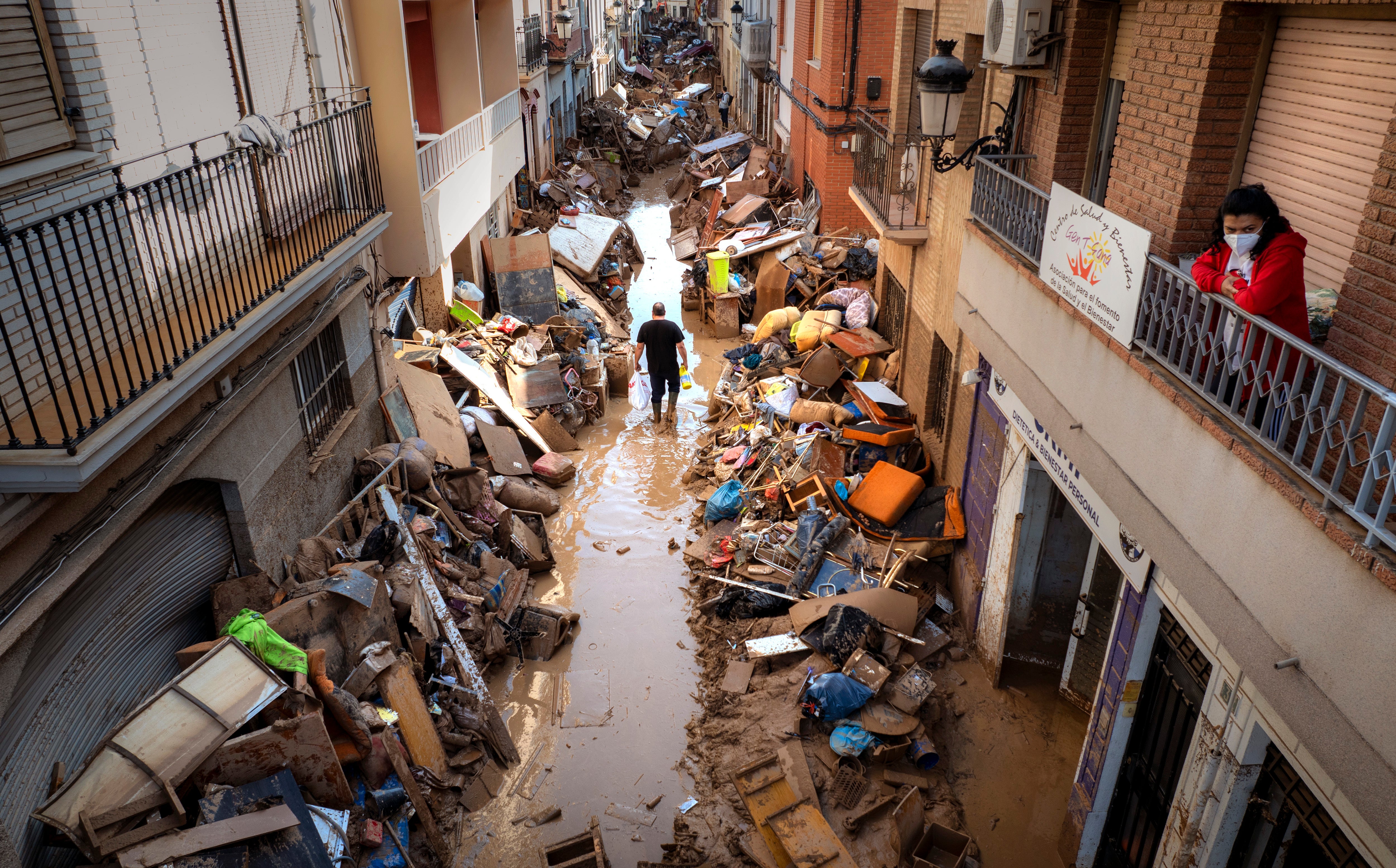 People walk through a street in Paiporta piled with broken furniture and debris