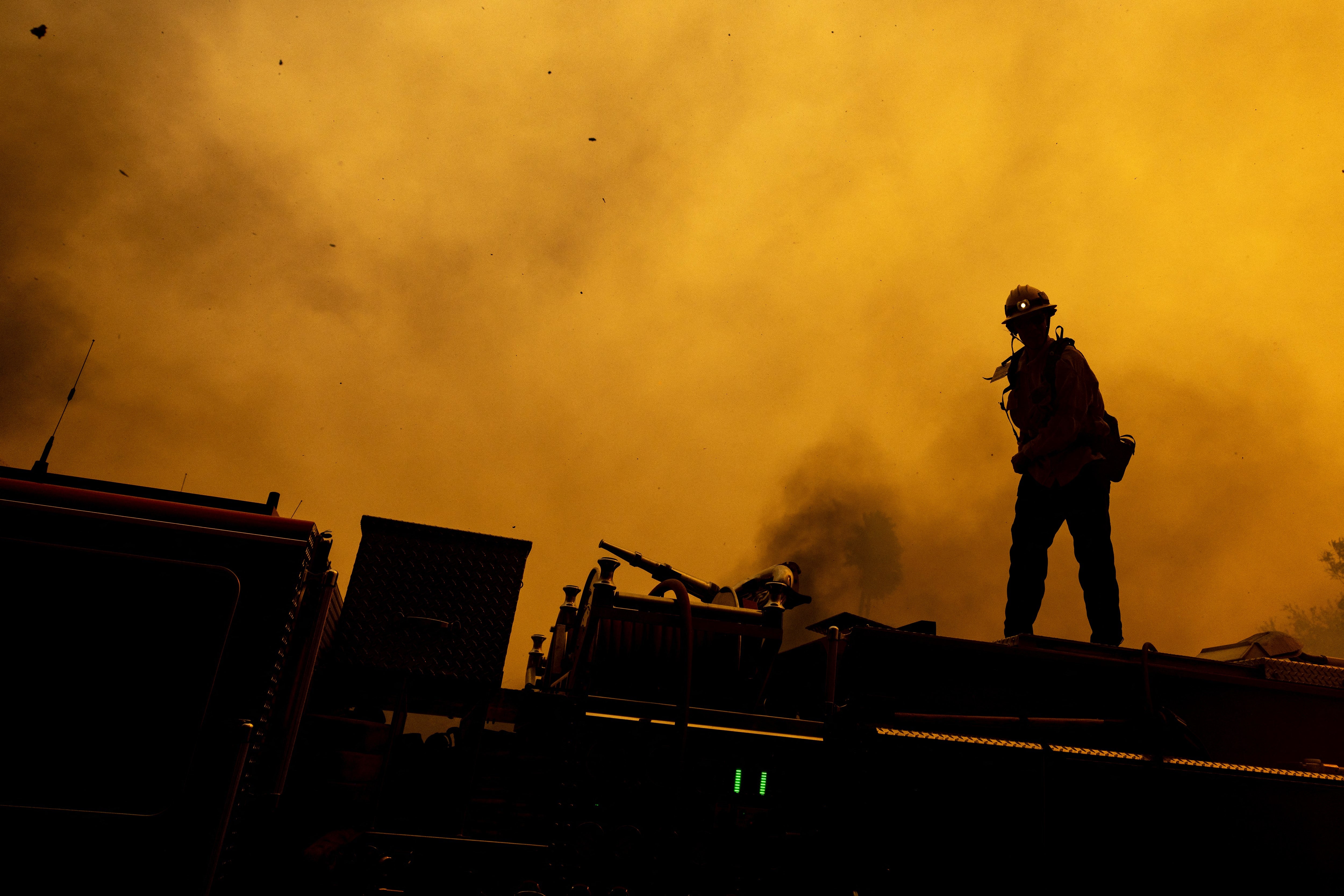 A firefighter stands on top of a fire truck, directing operations as the Mountain Fire scorches acres in Camarillo Heights, Camarillo, California. Climate change is thought to be worsening a number of environmental disasters across the US