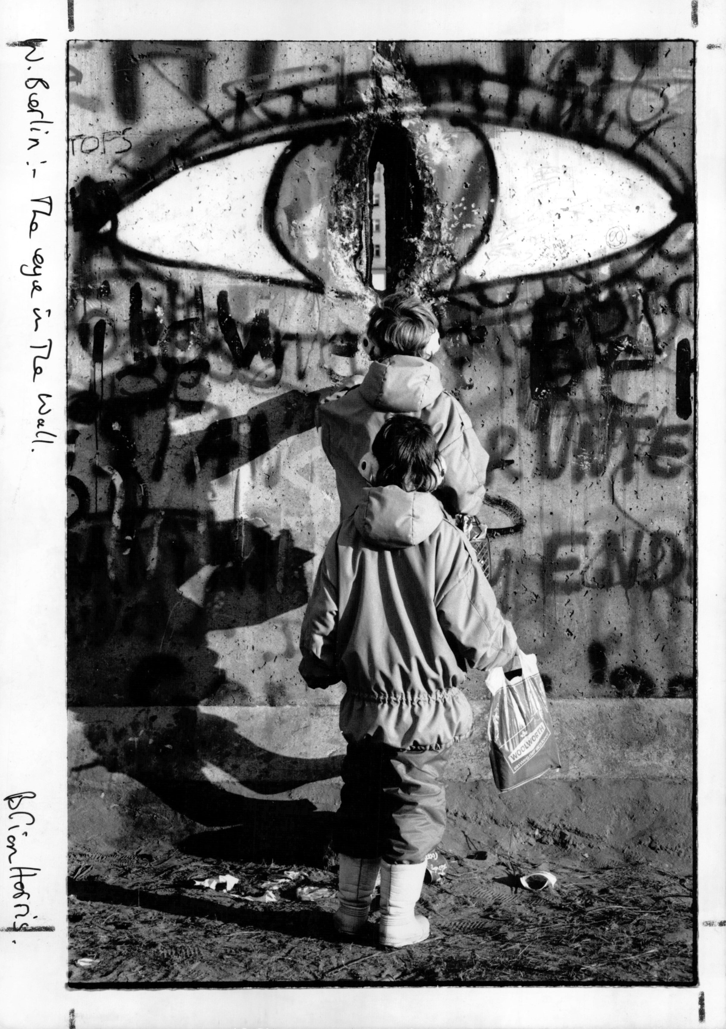 Eye in the wall: two kids peer through a hole in the wall