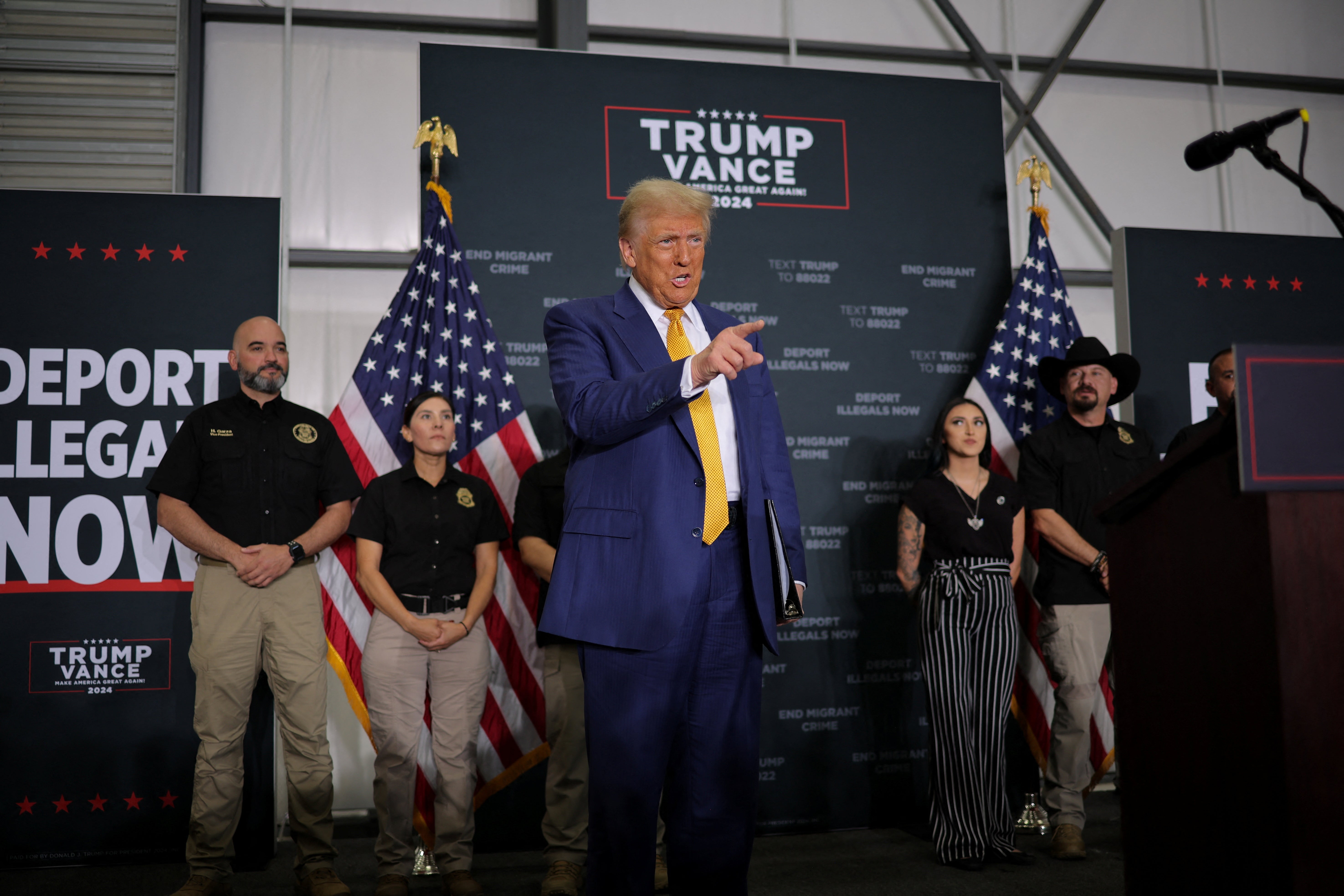 Donald Trump speaks to supporters in front of a poster reading ‘Deport Illegals Now’ on October 25