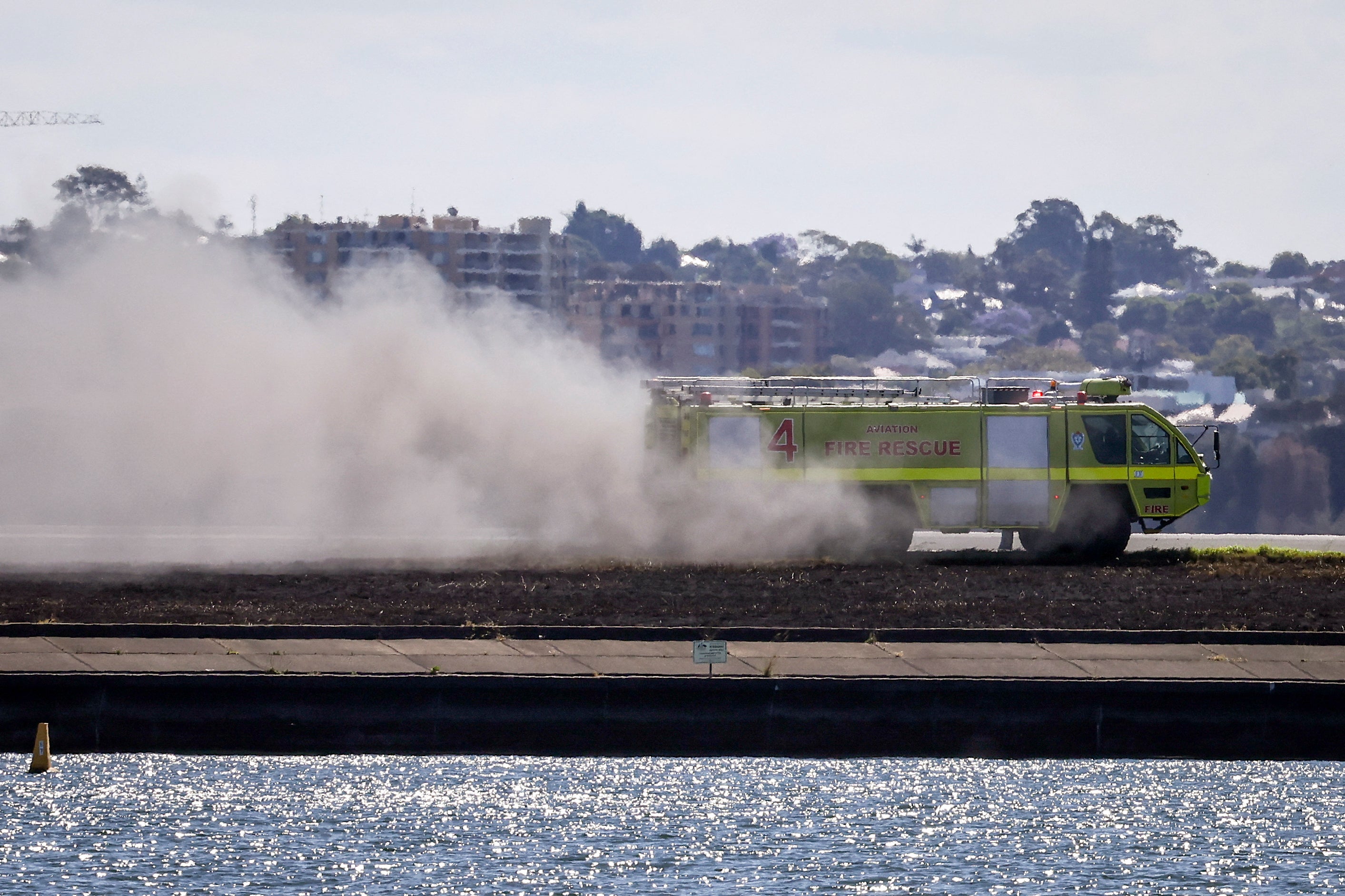 A truck sprays water where a grass fire occurred near a runway at Sydney International Airpor