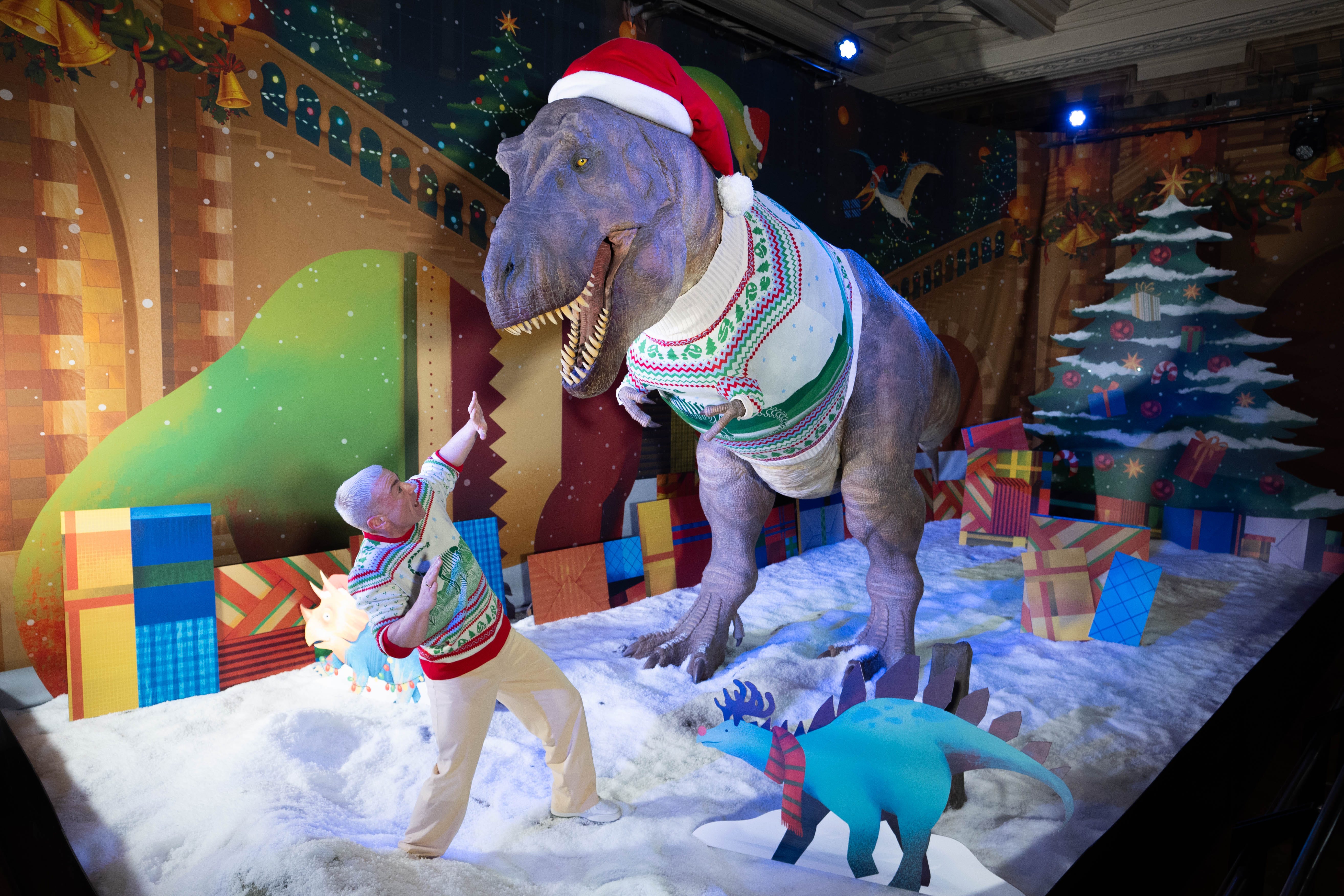 A member of staff poses with a T. rex at the unveiling of the Natural History Museum’s 2024 Christmas jumper (James Manning/PA)