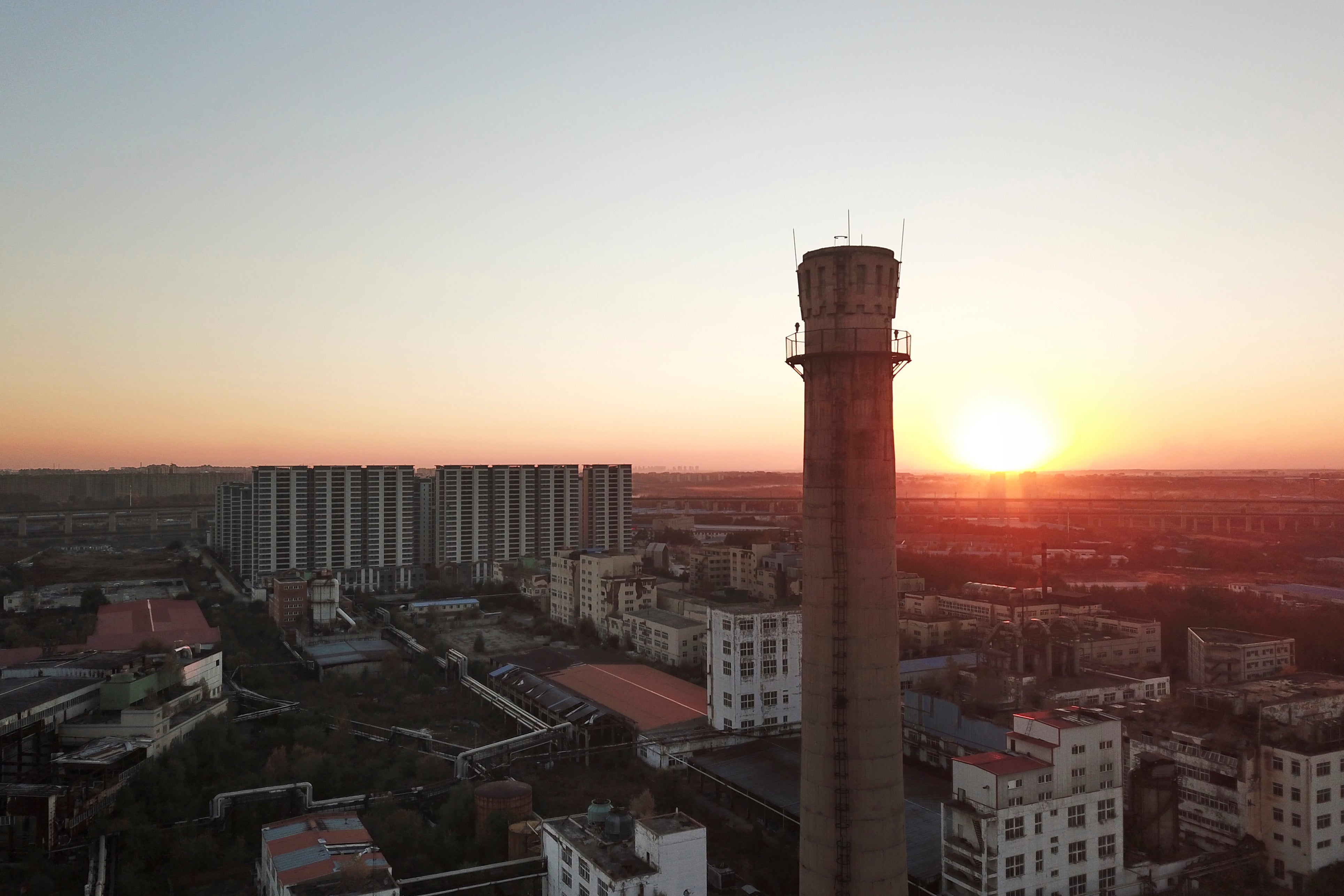 The sun sets near the smokestack of an abandoned factory of Dacheng Shenghua Feed company in Changchun