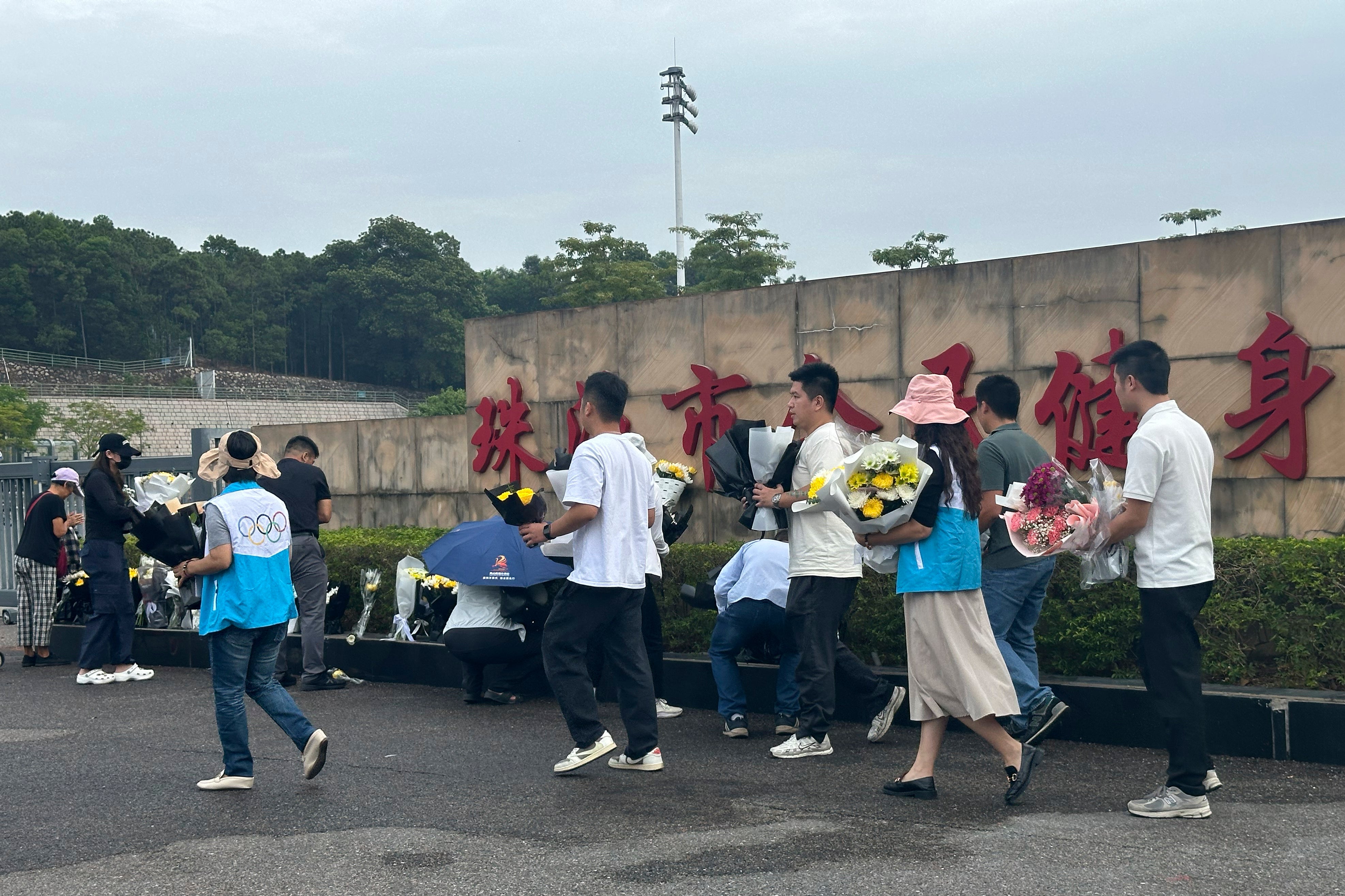 Volunteers relocate flowers laid outside the Zhuhai People’s Fitness Plaza to a barrier leading into the area where a man rammed his car into people