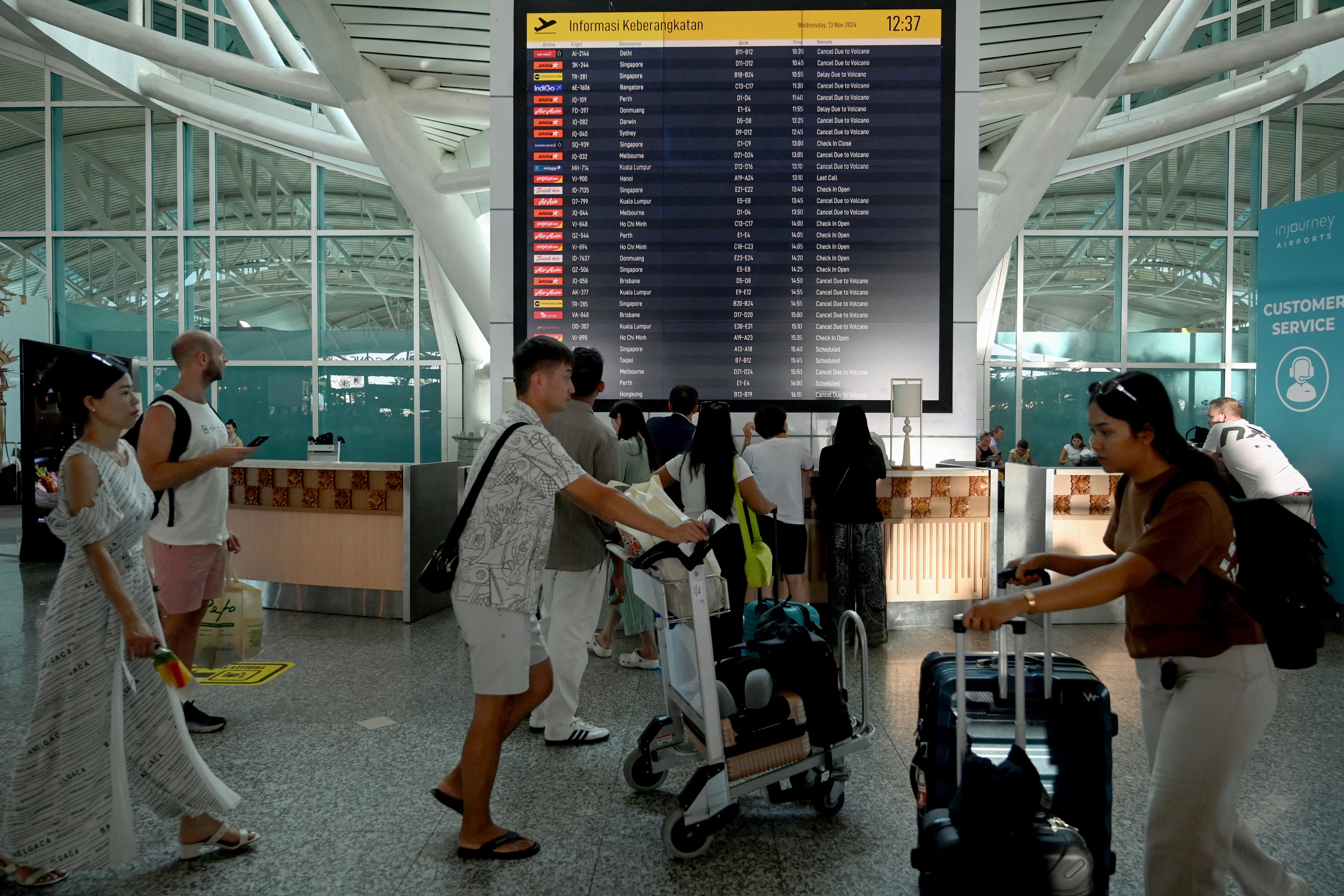 Passengers look at an electronic board displaying cancelled flights after the nearby Mount Lewotobi Laki-Laki volcano catapulted an ash tower