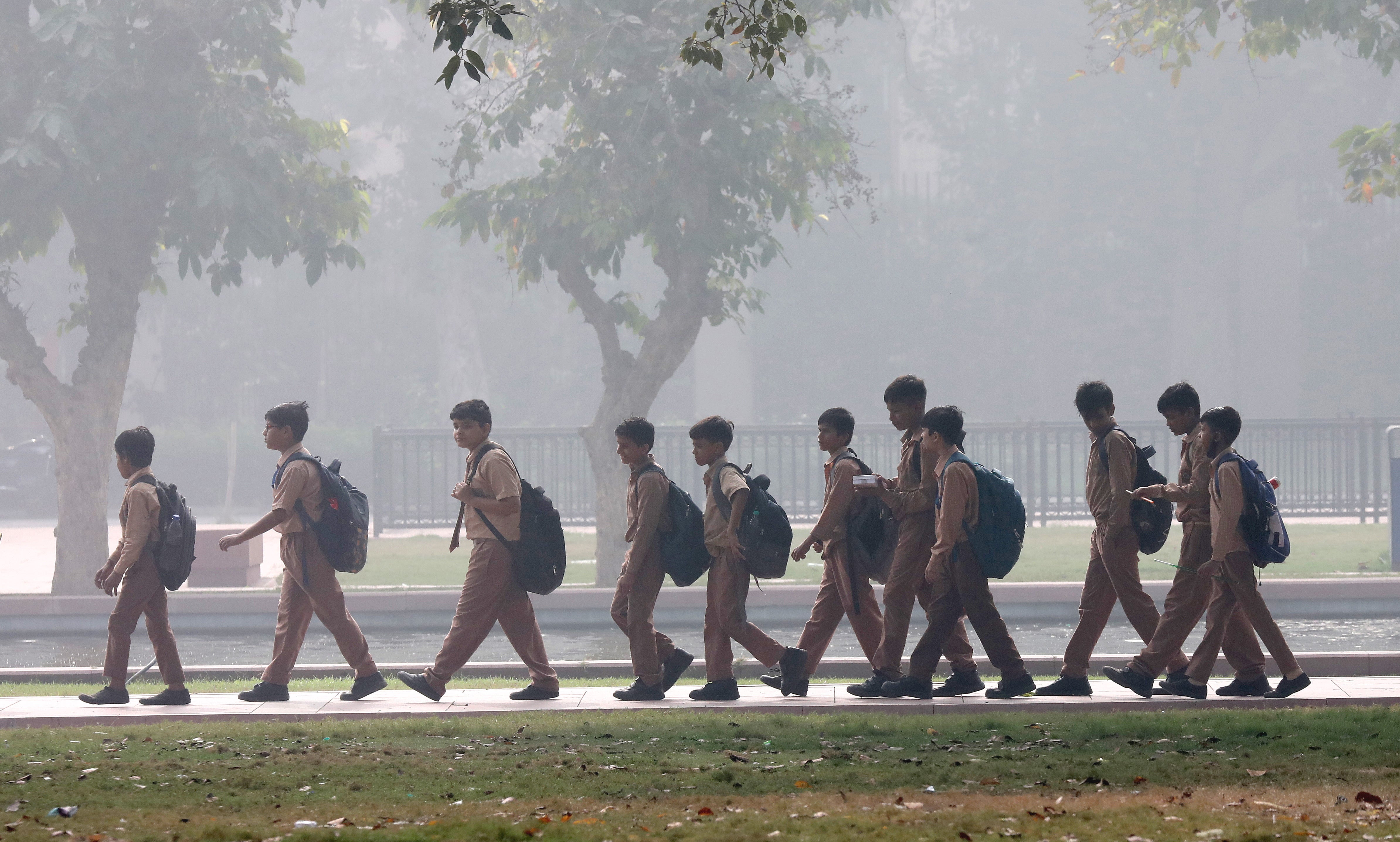 Schoolchildren walk along a street as Delhi is enveloped by smog on 14 November 2024