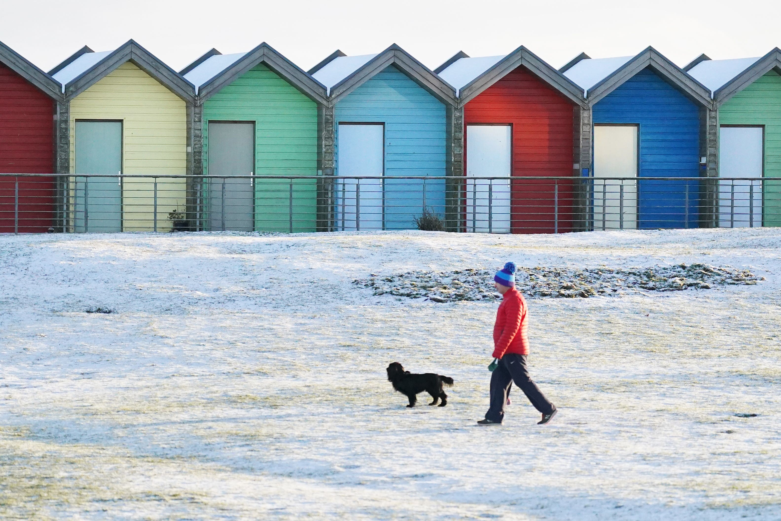 A man walks his dog near the beach huts on Blyth beach, Northumberland, on the north east coast (Owen Humphreys/PA)