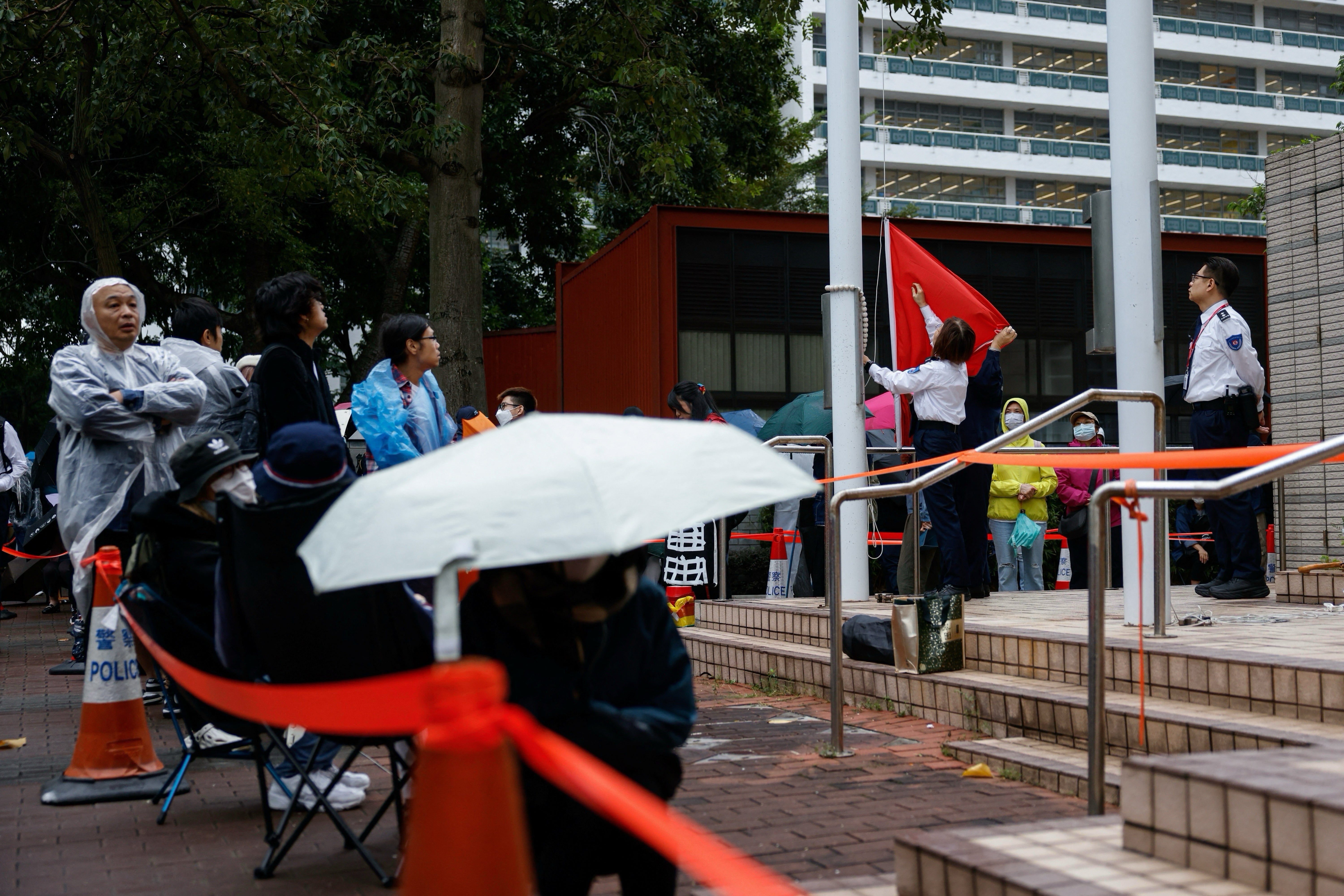 Court staff raise a national flag next to people queueing to enter the West Kowloon Magistrates Court before the sentencing of the 45 convicted pro-democracy activists