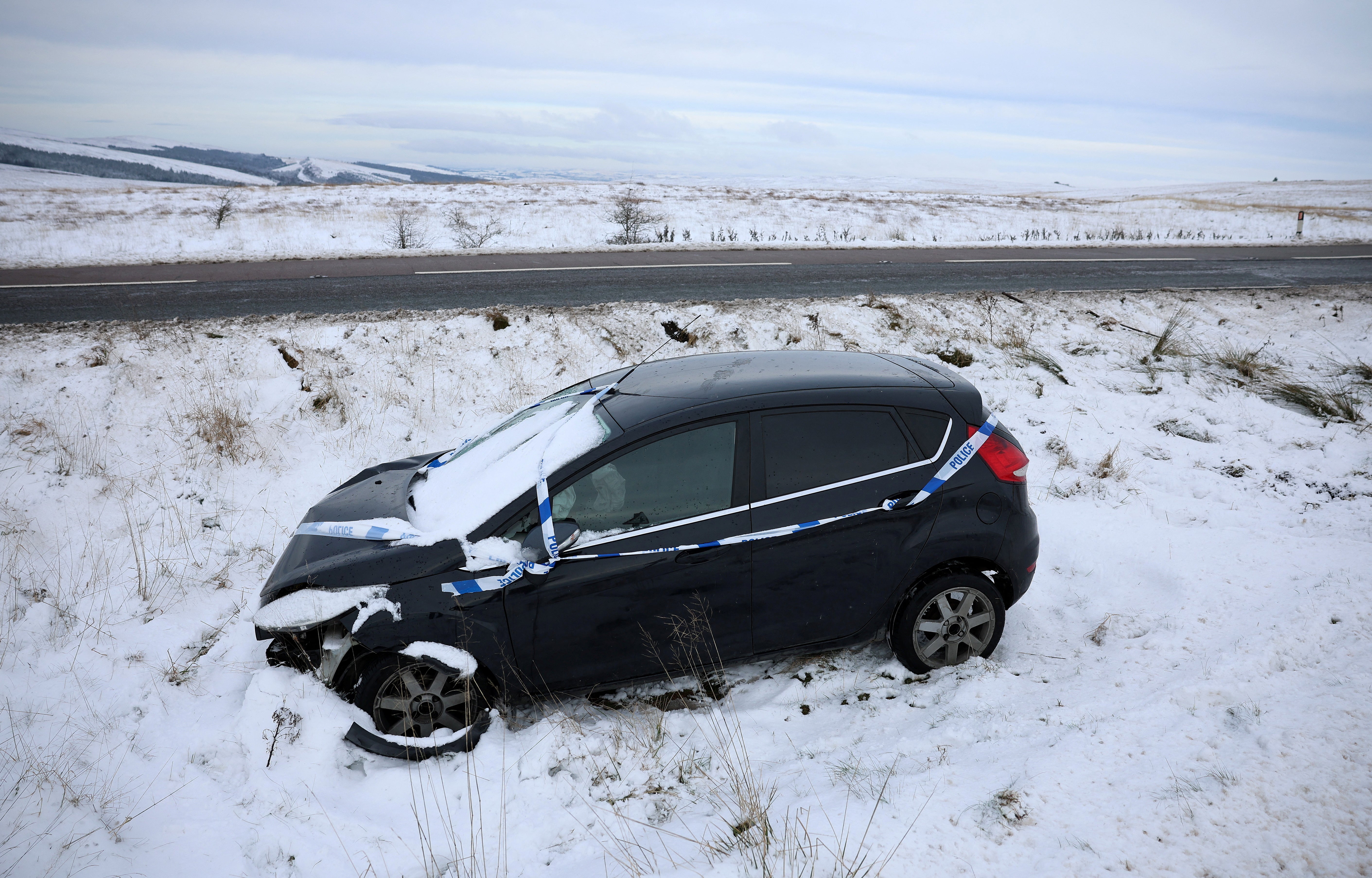 A crashed car lies covered in snow in a ditch at the side of a road near Buxton, Britain, following heavy snow in the Peak District