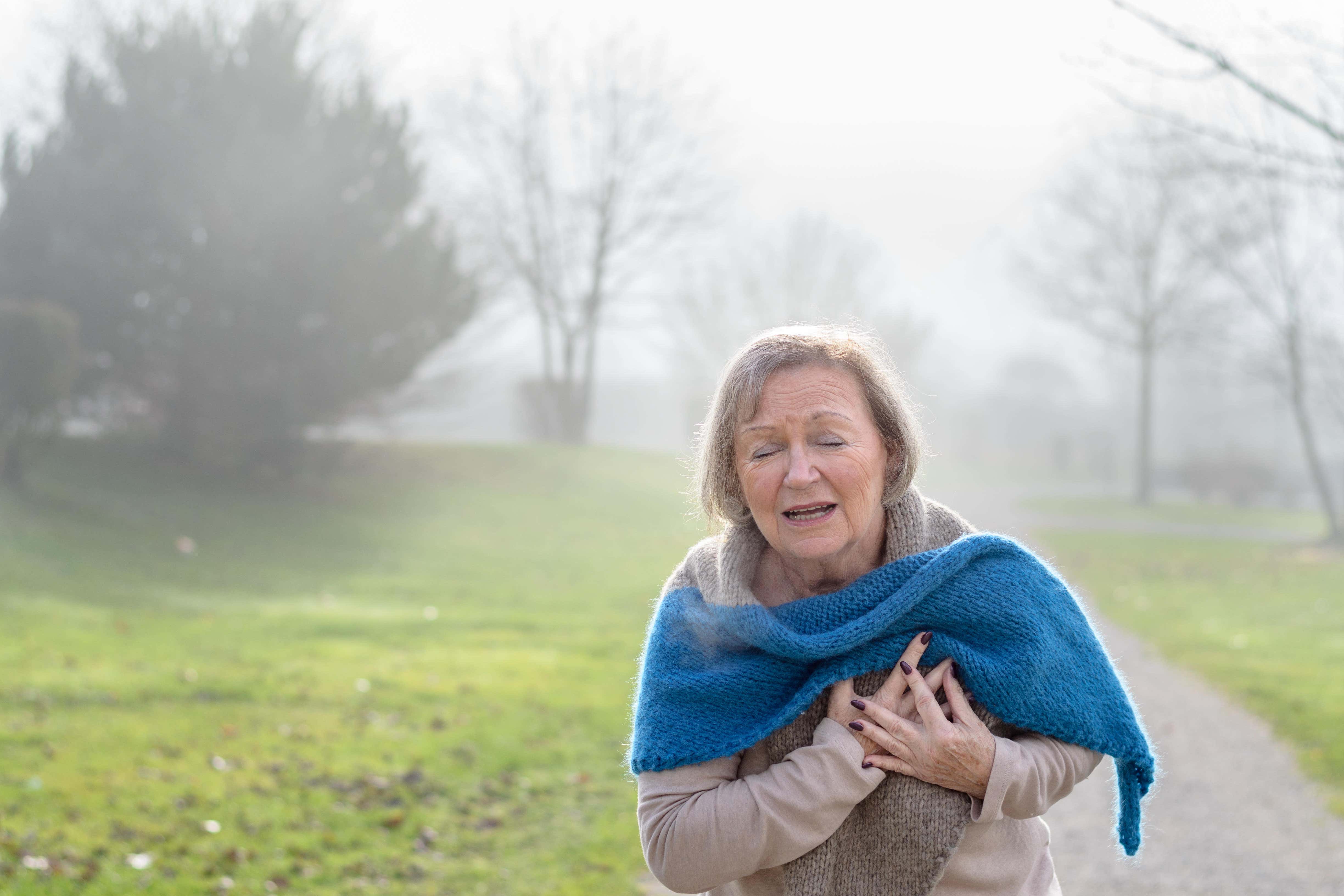 A lady clutching her chest in pain at the first signs of angina or a myocardial infarct or heart attack