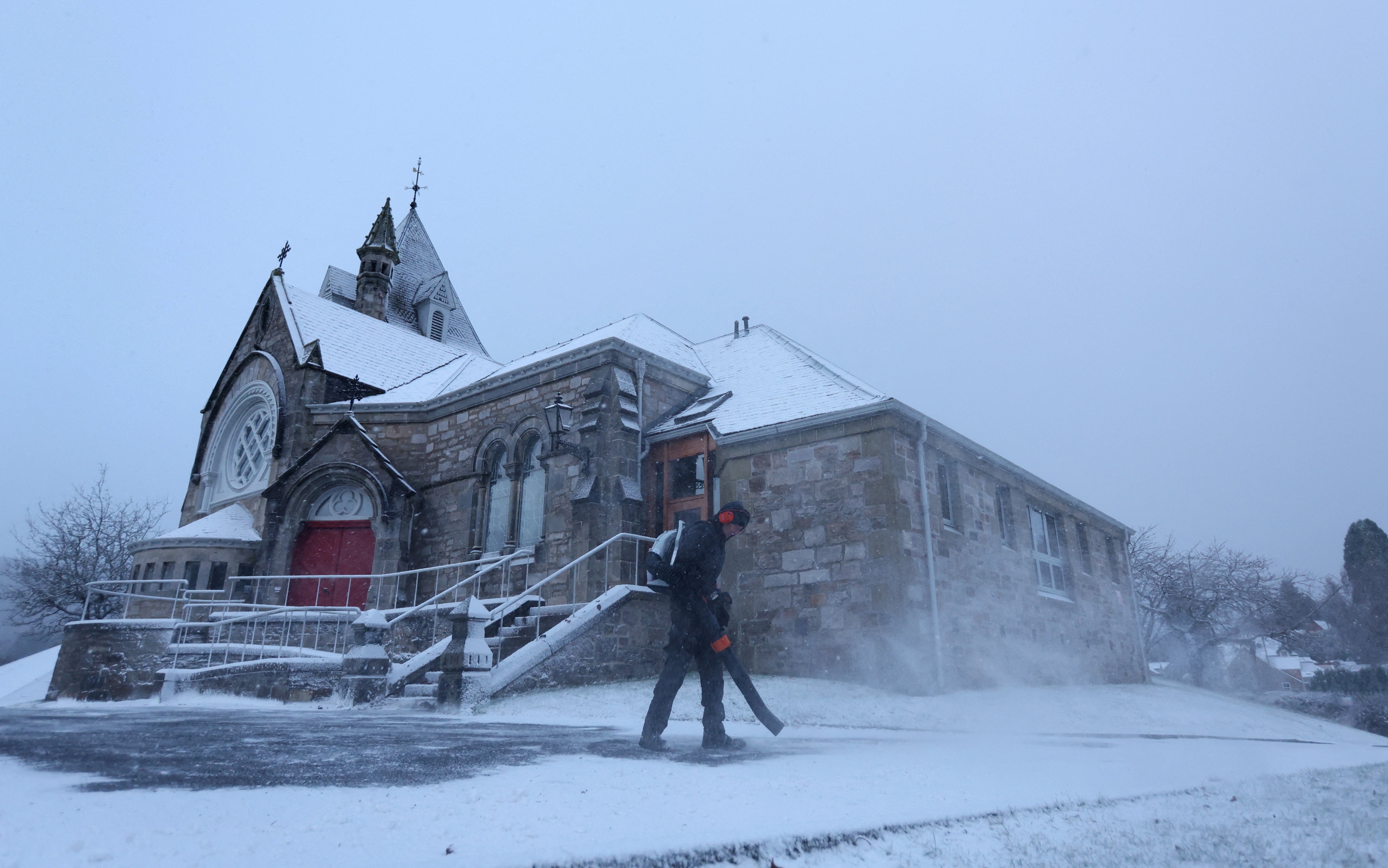 A man clears snow at the Church of Scotland in Pitlochry, Scotland