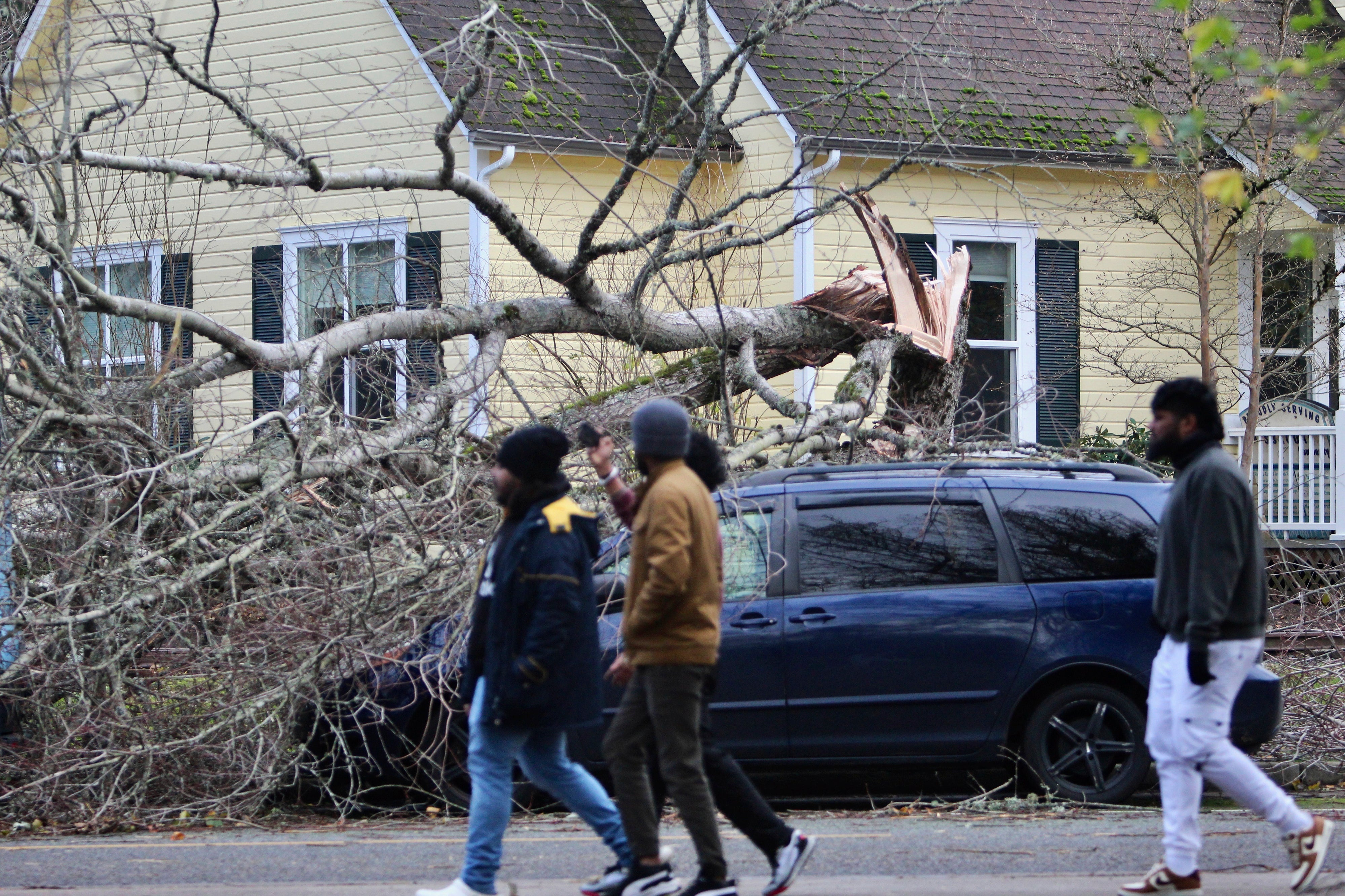 People walk by a minivan hit by a tree that fell during a bomb cyclone storm in Issaquah, Washington on Wednesday