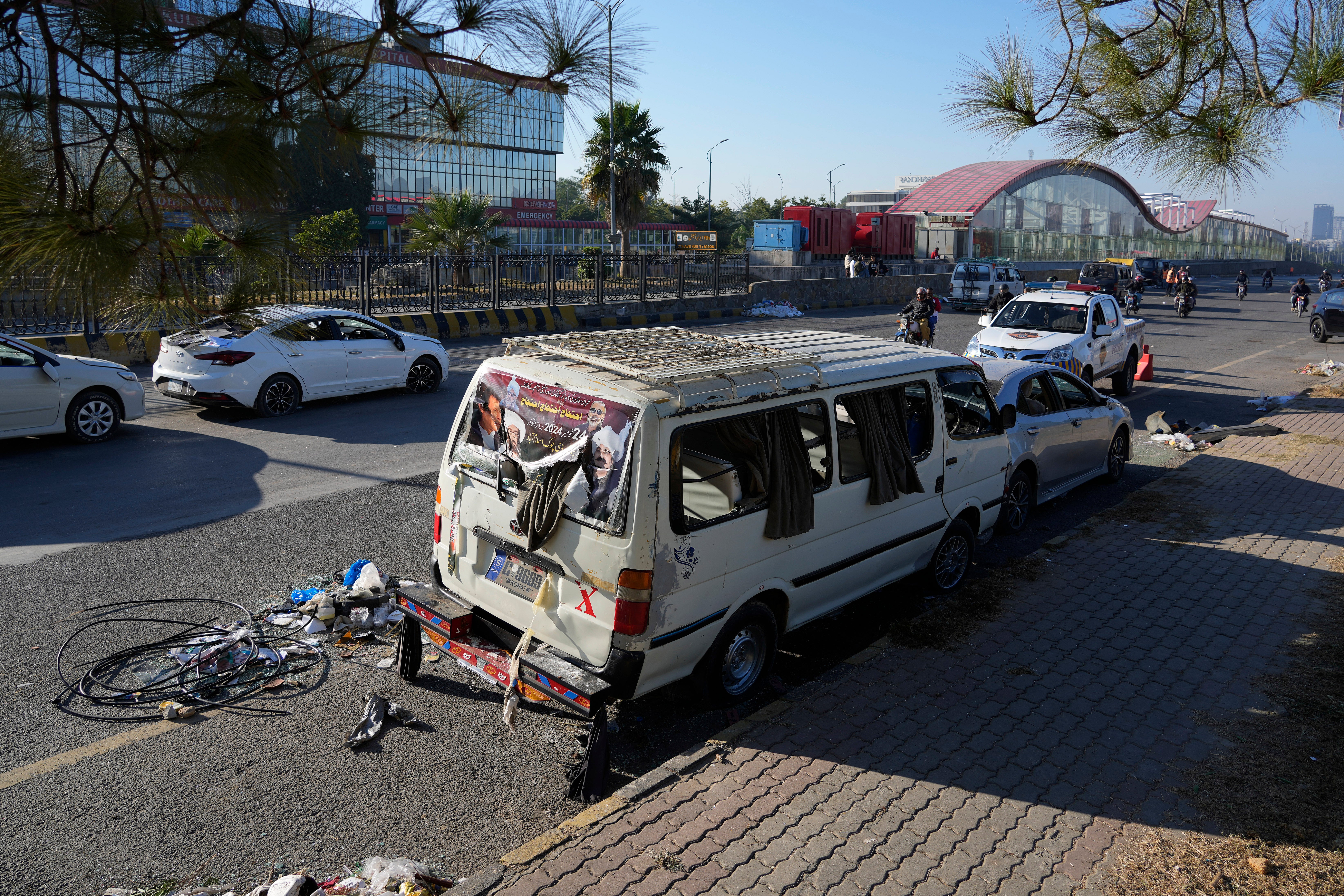 A motorcyclist drives through the damaged vehicles left behind by supporters of Khan