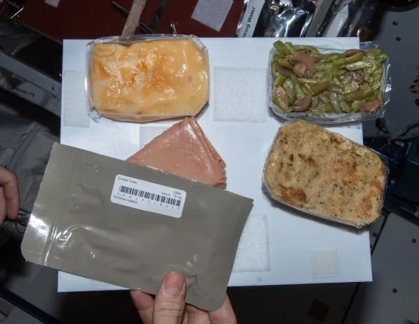 A close-up shot shows the Thanksgiving dinner items on the space station in 2013. The food includes turkey, ham, macaroni and cheese, green beans and mushrooms, and dressing