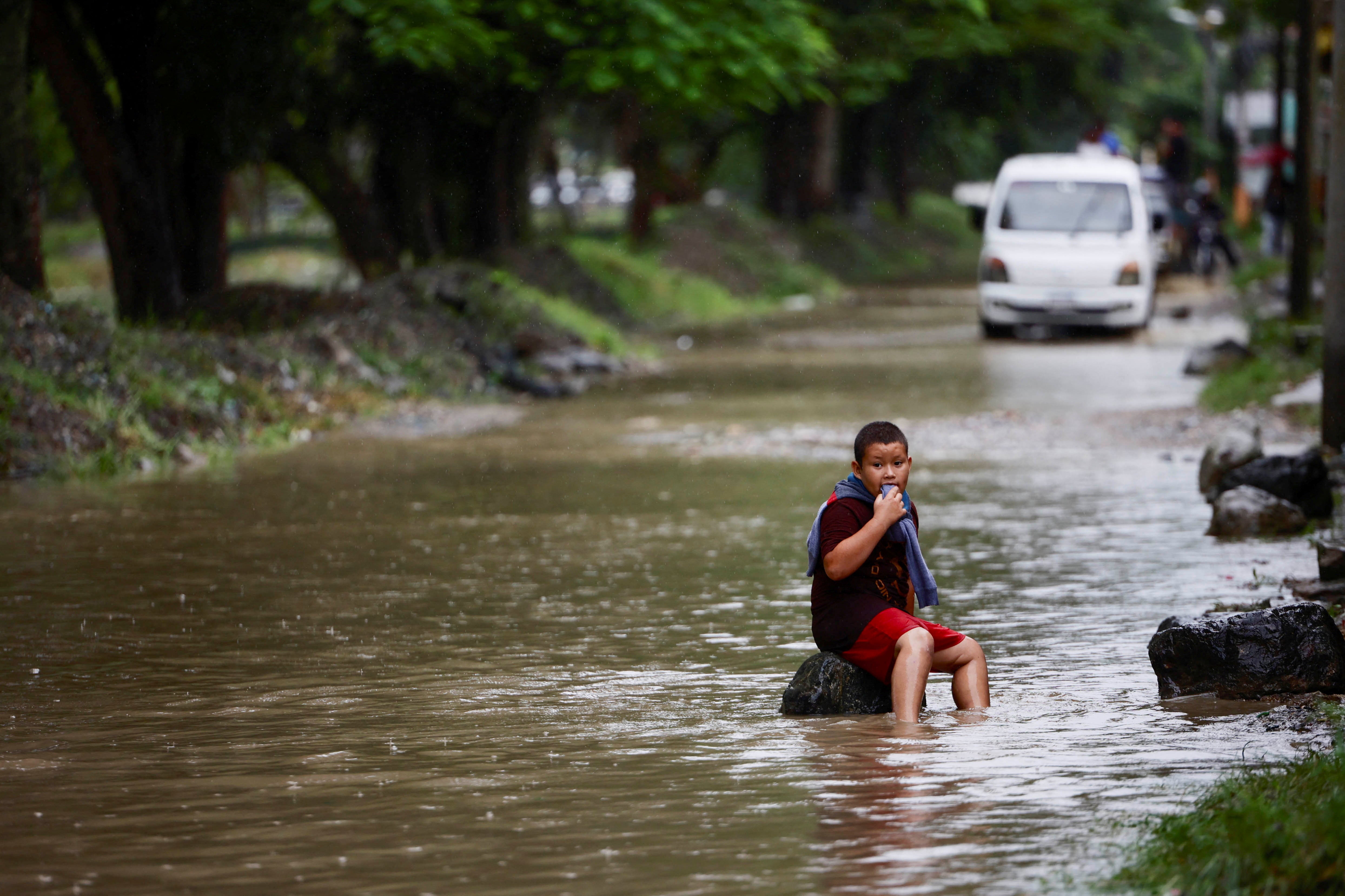 A child sits on a rock in a flooded street following Tropical Storm Sara, in El Progreso, Honduras, earlier this month. The storm had been forecast to swing toward the Gulf Coast, but stalled over Central America instead