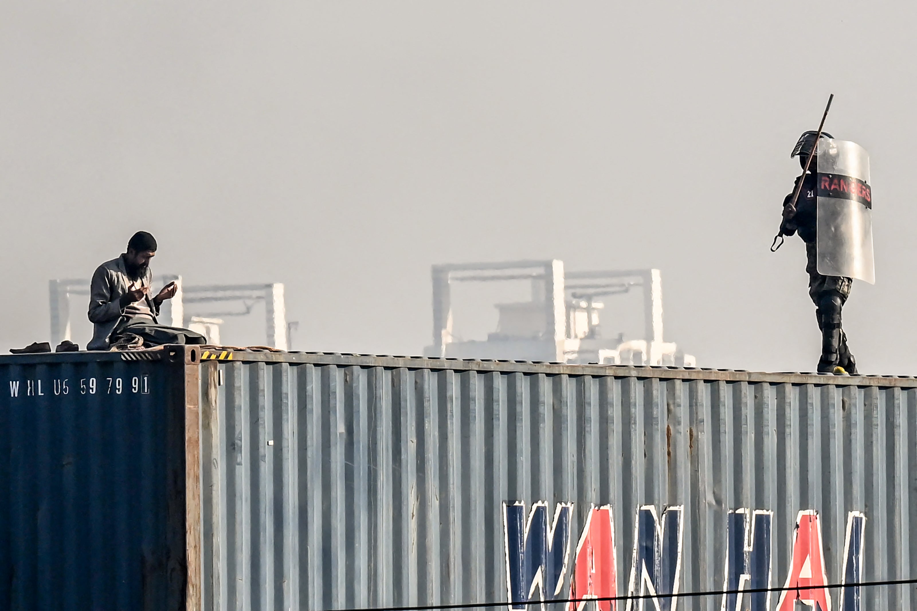 A supporter of the Pakistan Tehreek-e-Insaf (PTI) party offers prayers on top of a shipping container as a paramilitary soldier chases him