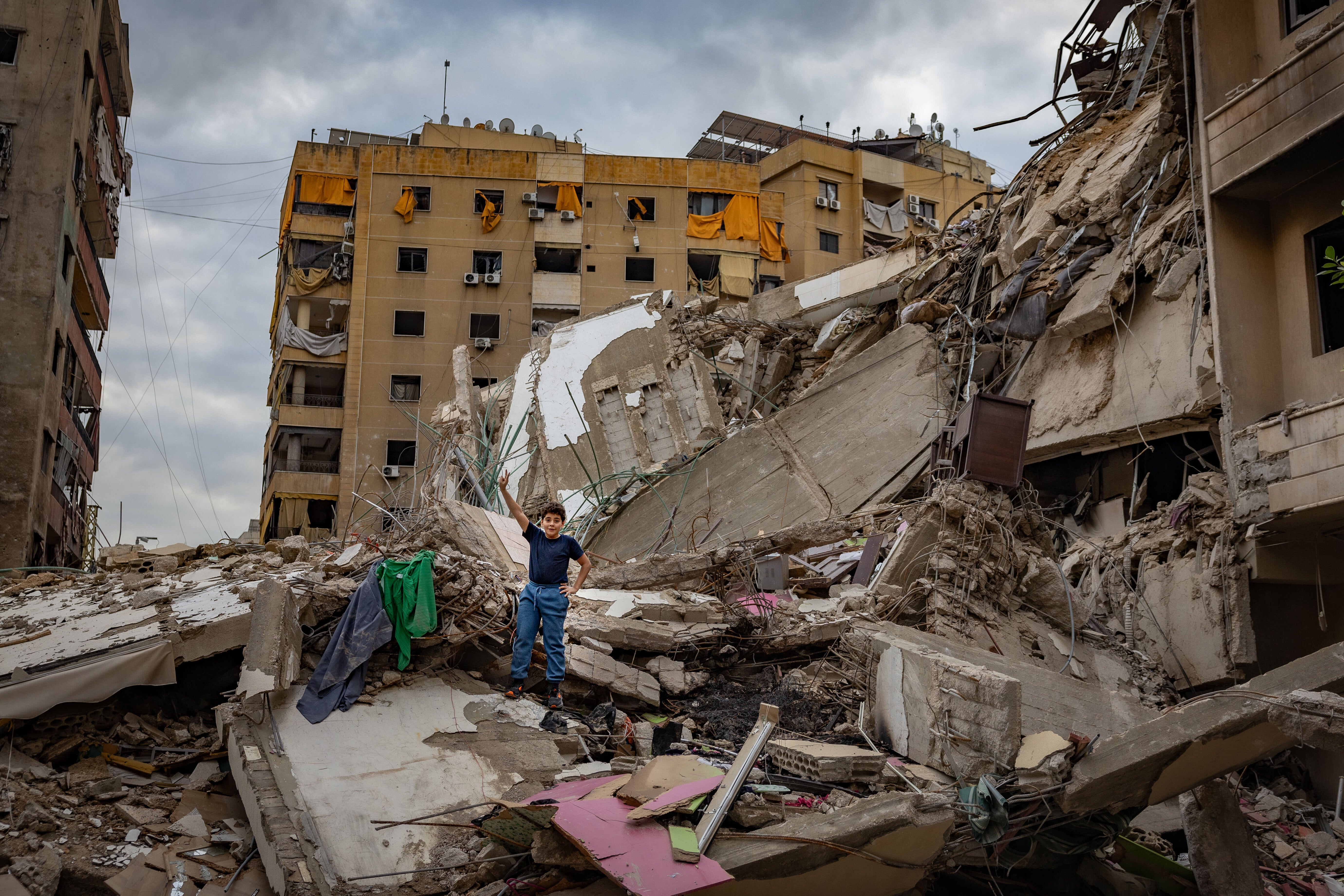 A boy makes a ‘V is for victory’ hand signal on a destroyed apartment building in one of the hardest-hit areas of Dahiyeh