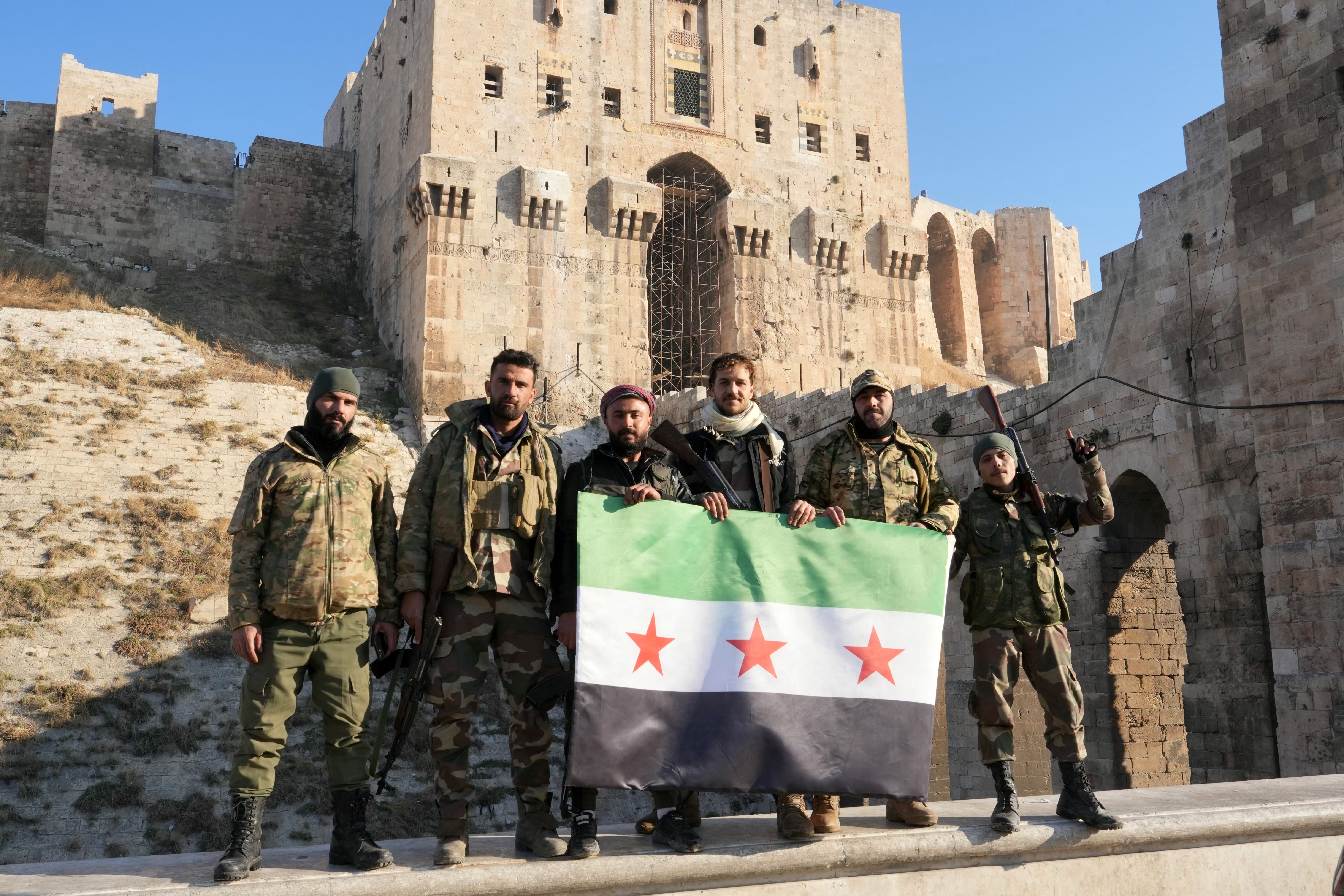 Anti-government fighters hold an opposition flag as they pose for a picture at the entrance of the citadel in Aleppo