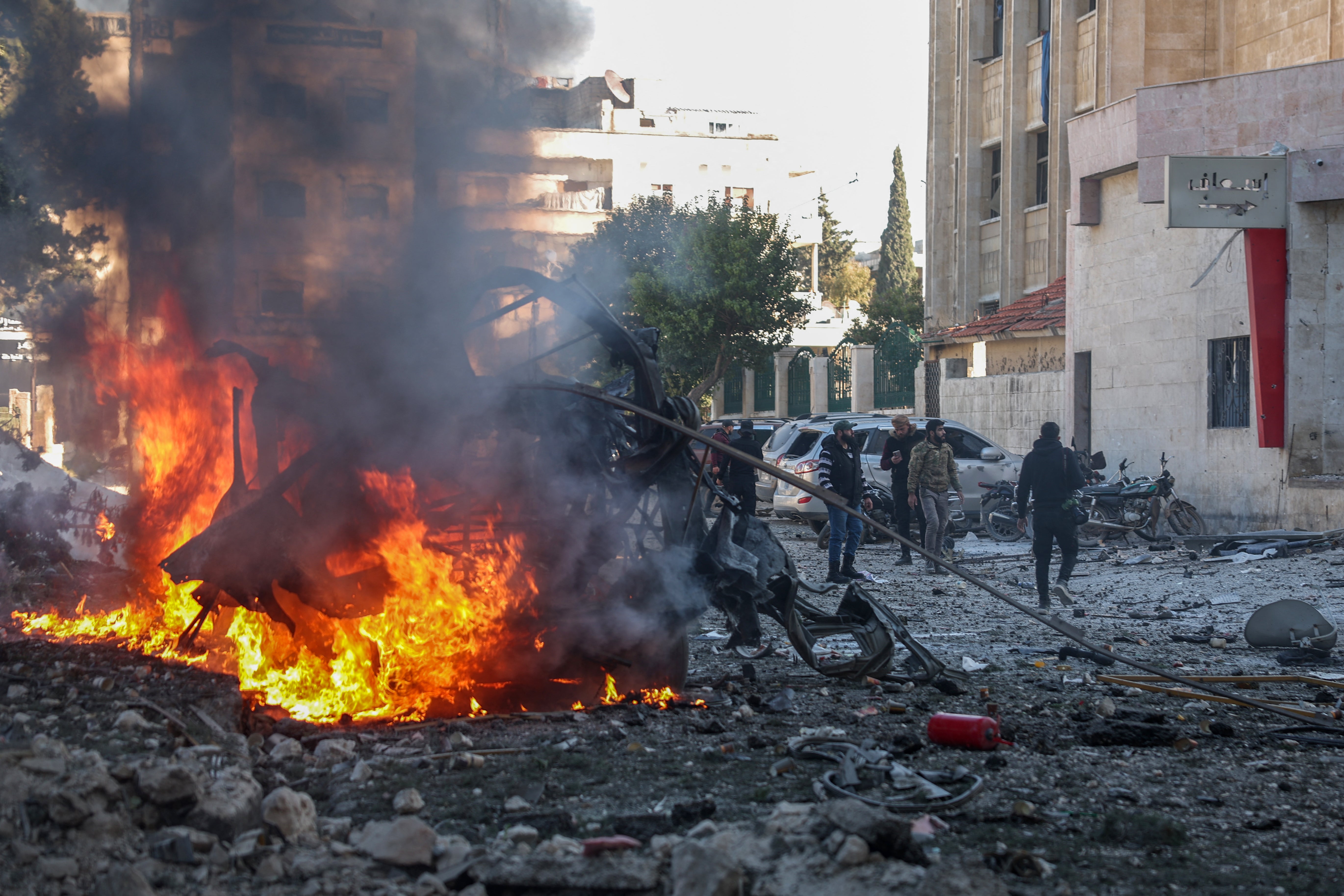 People stand near a burning car at the site of an airstrike that targeted Syria's rebel-held northern city of Idlib