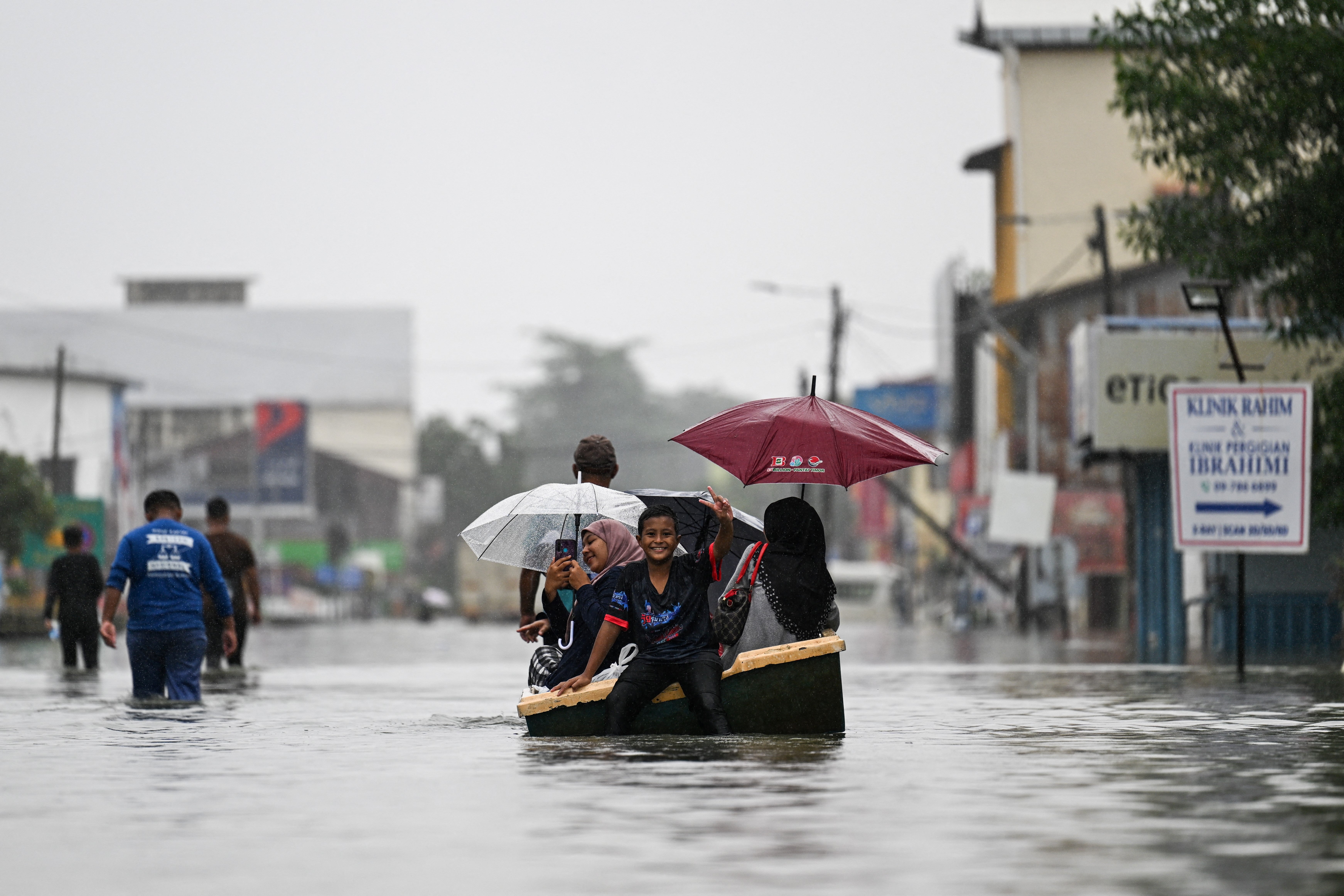 People use a boat through a flooded street during heavy rain in Pasir Puteh, Malaysia, on 30 November 2024