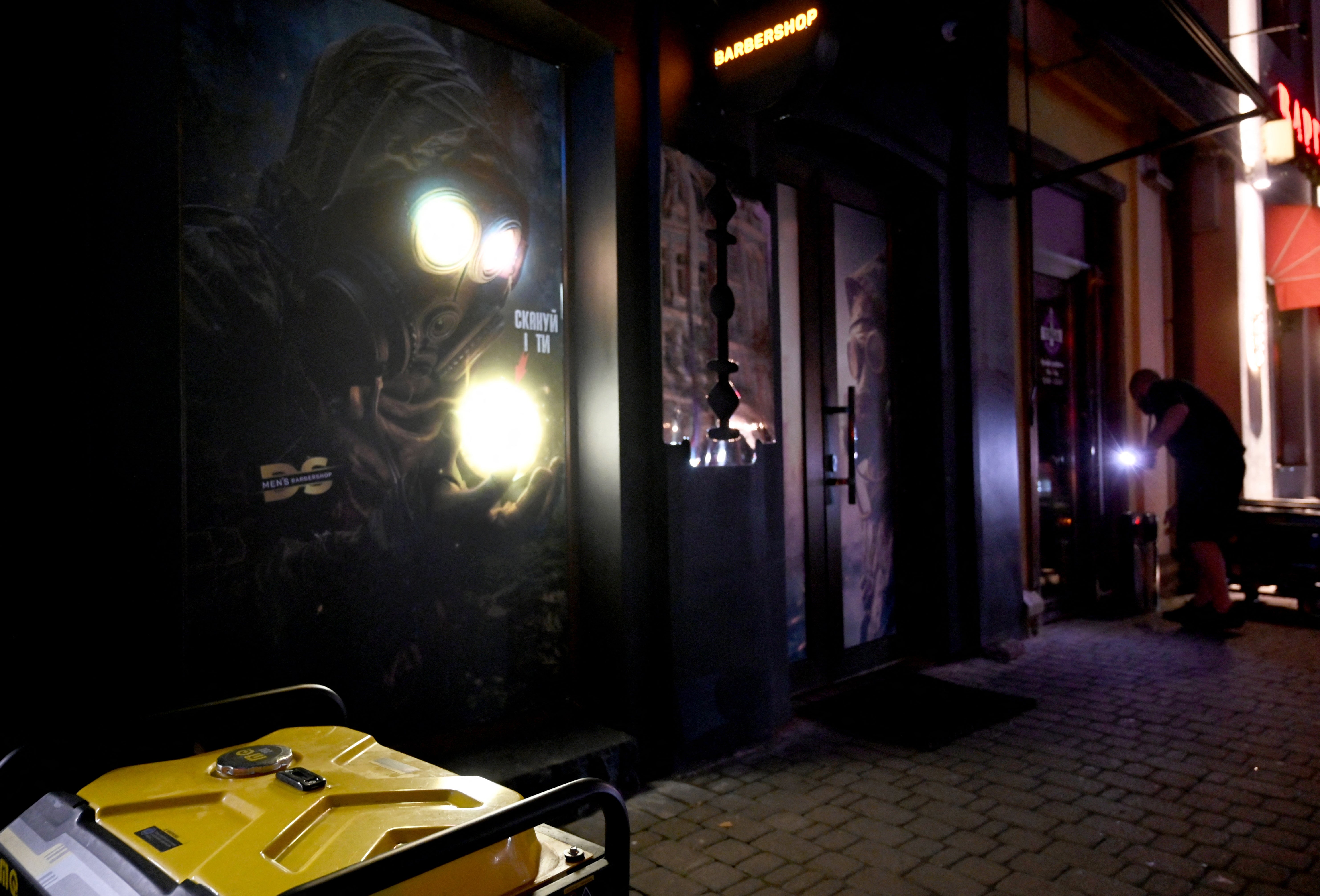 An employee with a flashlight installs a power generator outside a cafe during a partial blackout in Kyiv