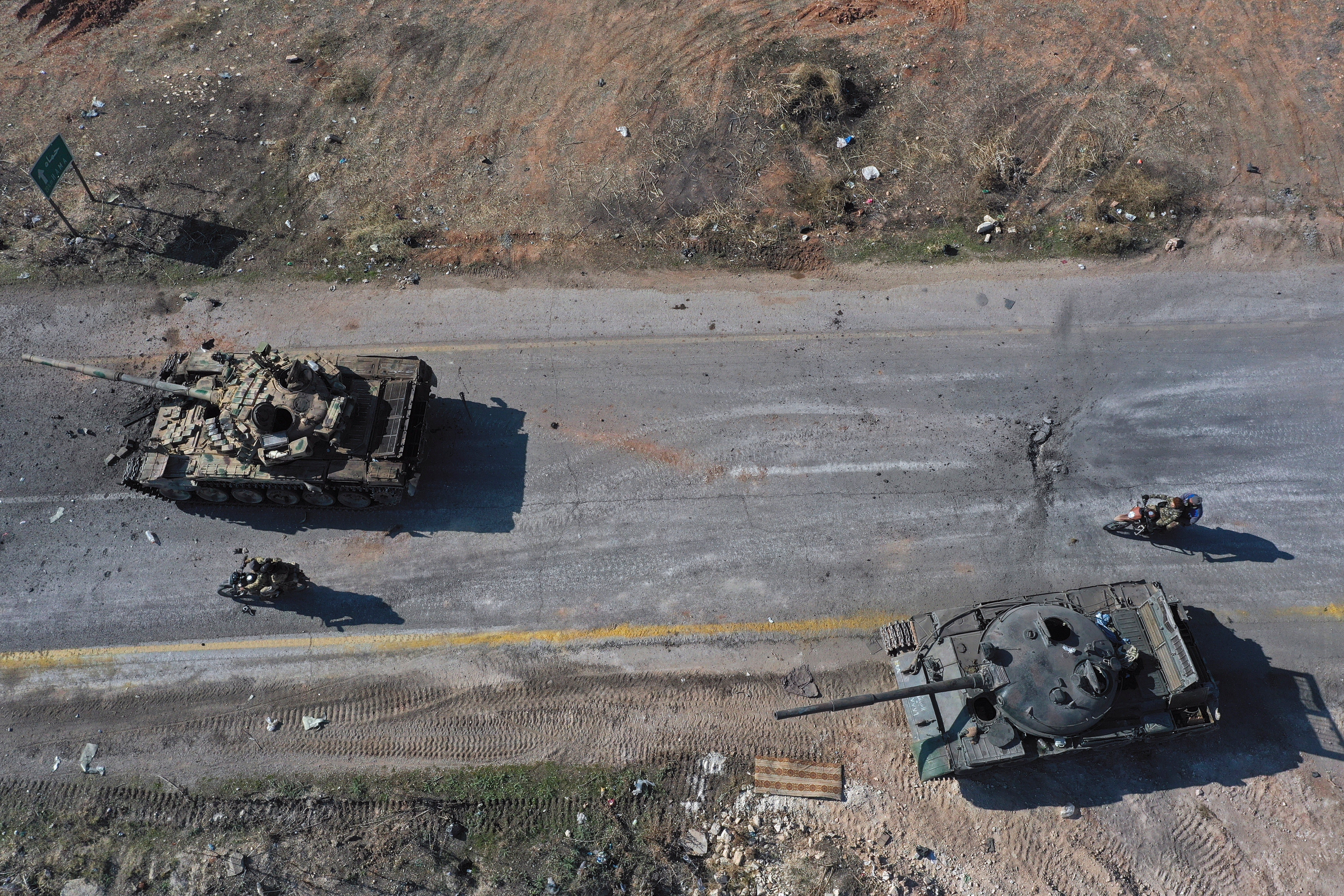 Syrian insurgents ride on motorcycles through abandoned Syrian army vehicles on a road in the outskirts of Hama