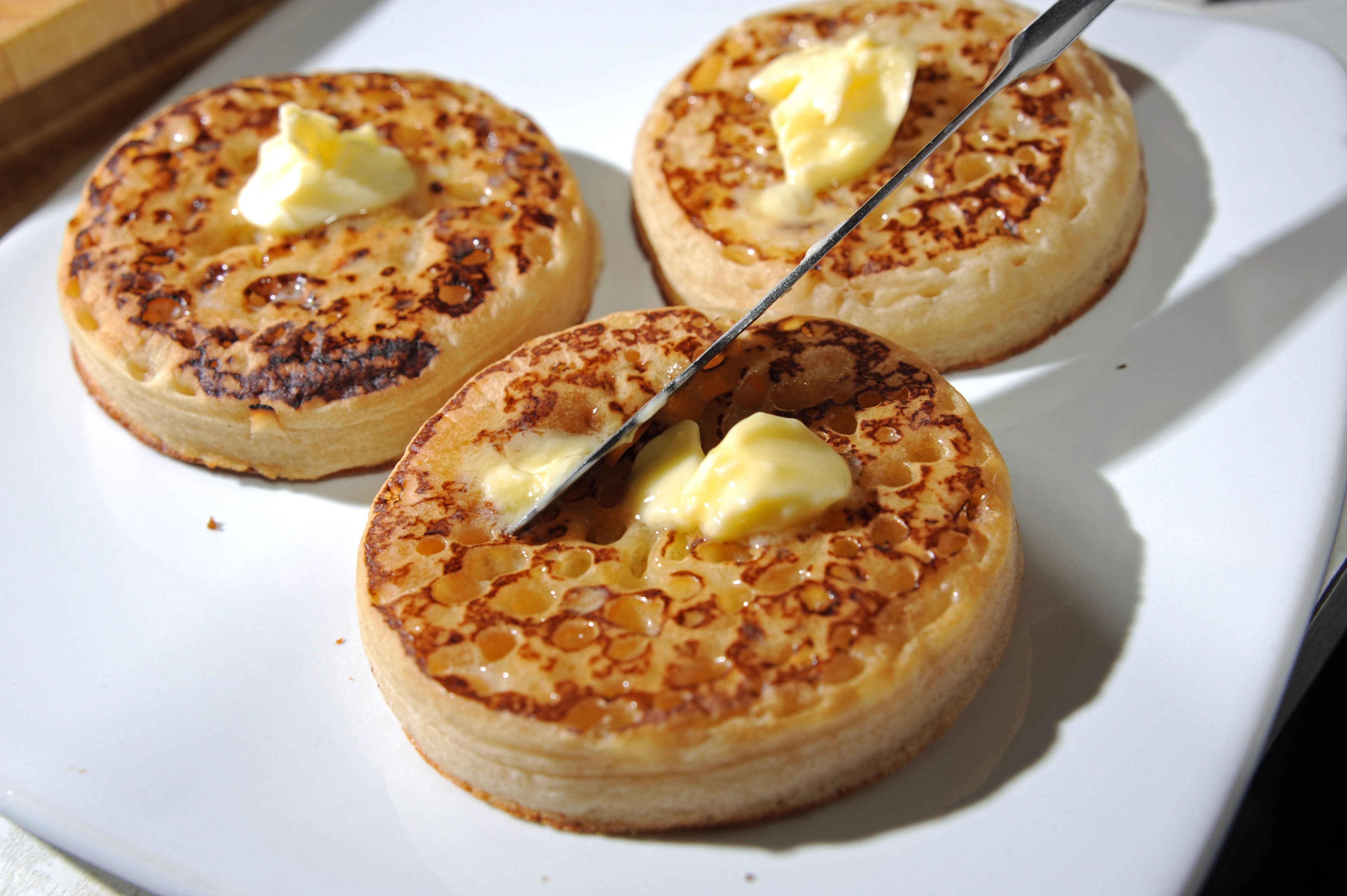 Spreading butter with a knife on a hot toasted crumpet for breakfast or tea